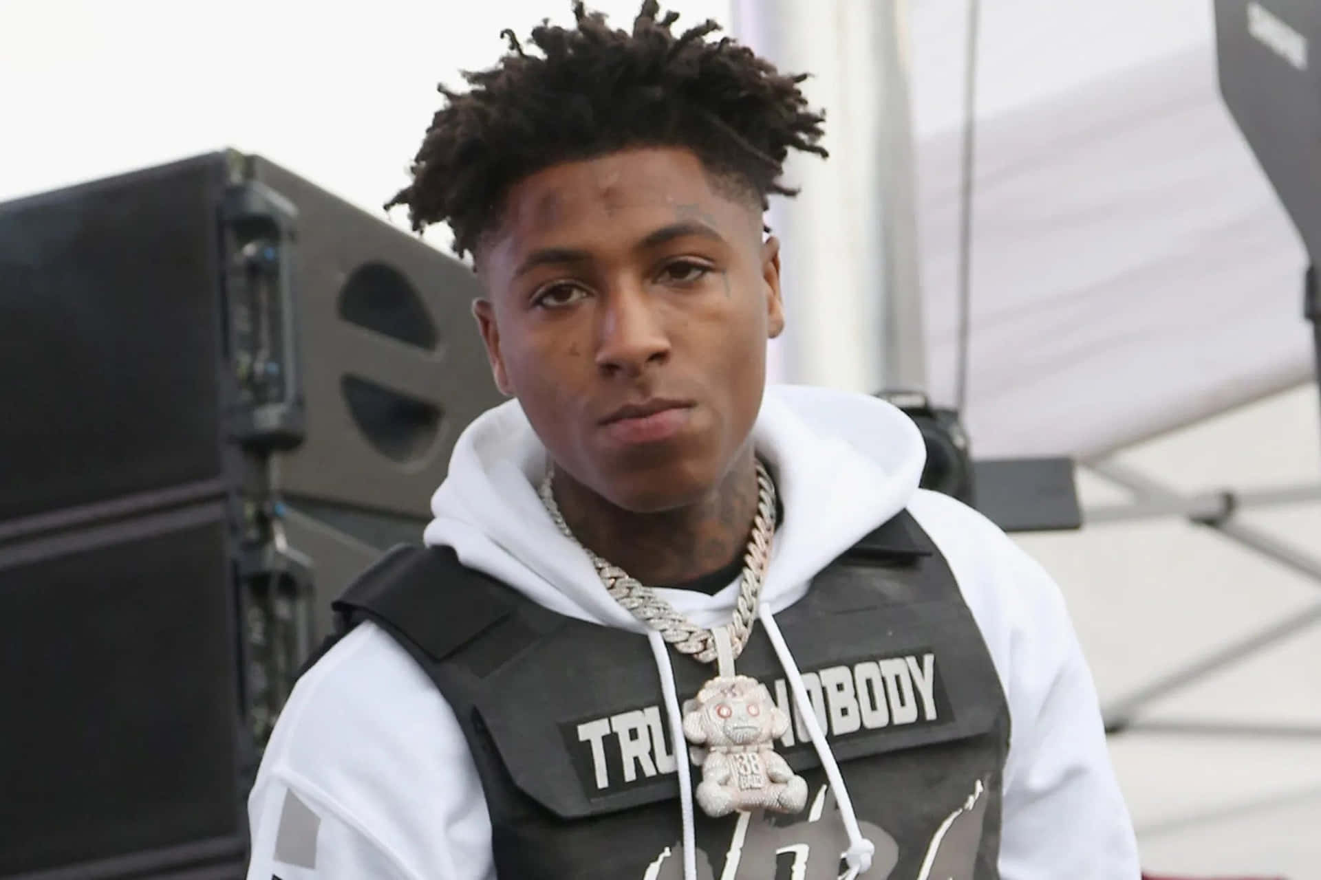 年輕男子穿著街頭風連帽衫和背心，搭配泰迪熊吊墜項鍊。 — NBA Youngboy 壁紙