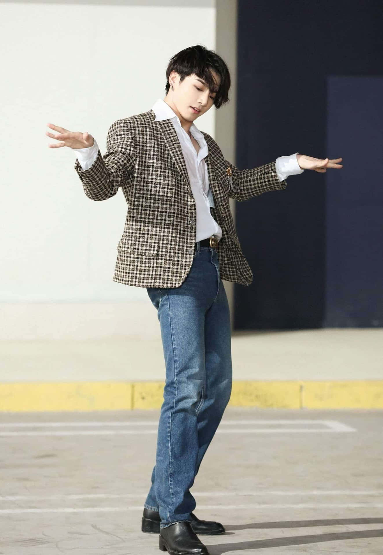 年輕男子穿著格紋西裝外套和牛仔褲在戶外跳舞。 — Jungkook 壁紙