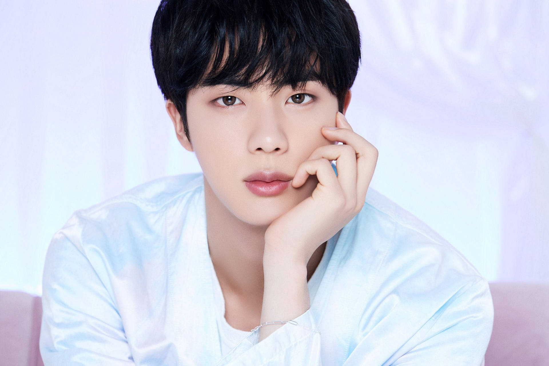 身穿淺藍色襯衫的年輕男子將下巴擱在手上，背景柔和。 — Bts 壁紙