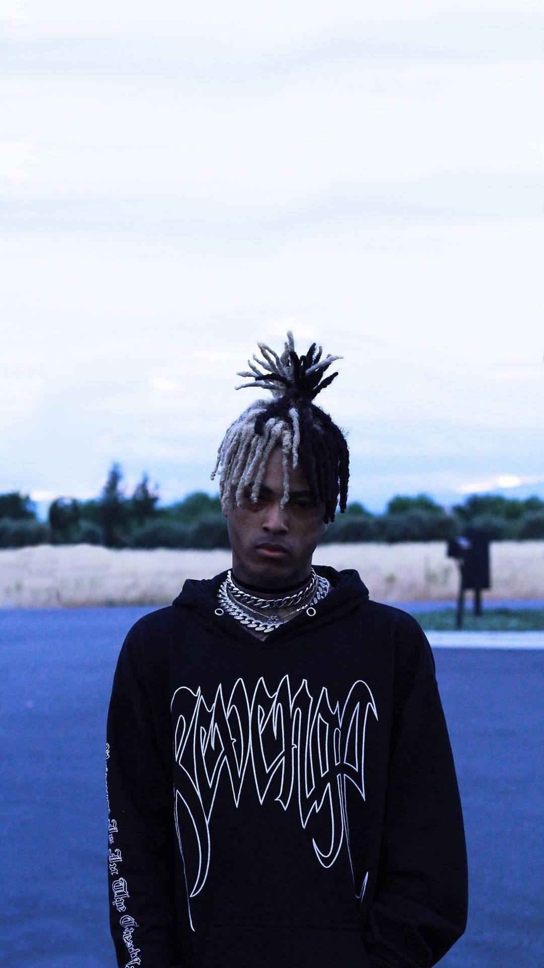 年輕男子編著辮子，戴著多層鏈條，在黃昏時分站在戶外。 — Xxxtentacion 壁紙