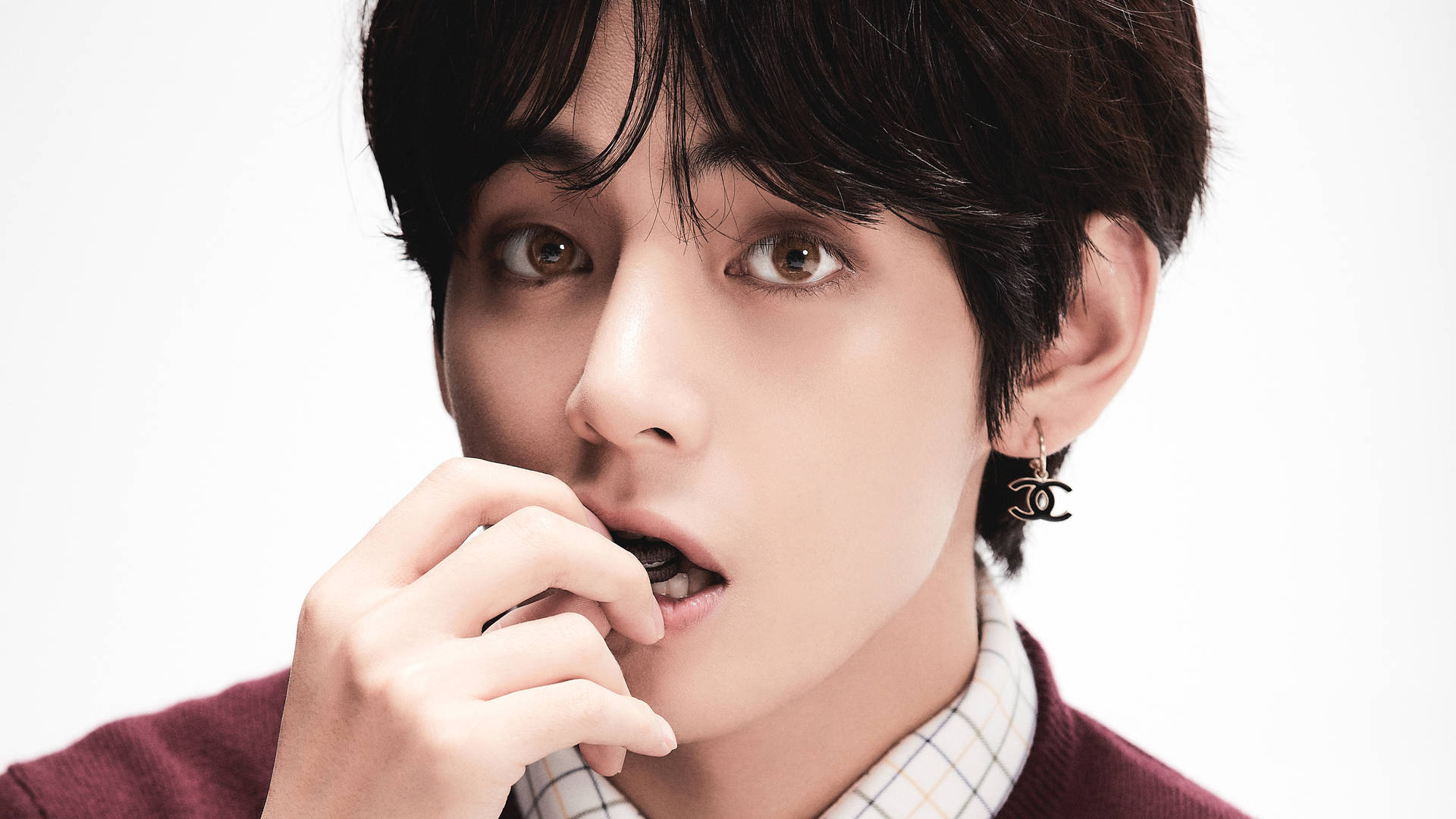 深色頭髮、戴著 Chanel 耳環的年輕男子在工作室肖像中咬手指。 — Jungkook 壁紙