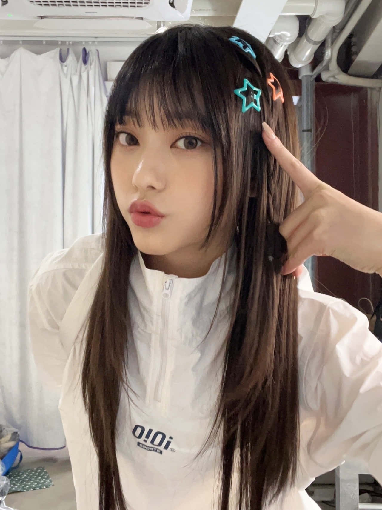  壁紙 — 一位年輕女性，長長的黑髮上裝飾著彩色星星髮夾，穿著白色拉鍊外套，在室內俏皮地擺姿勢。