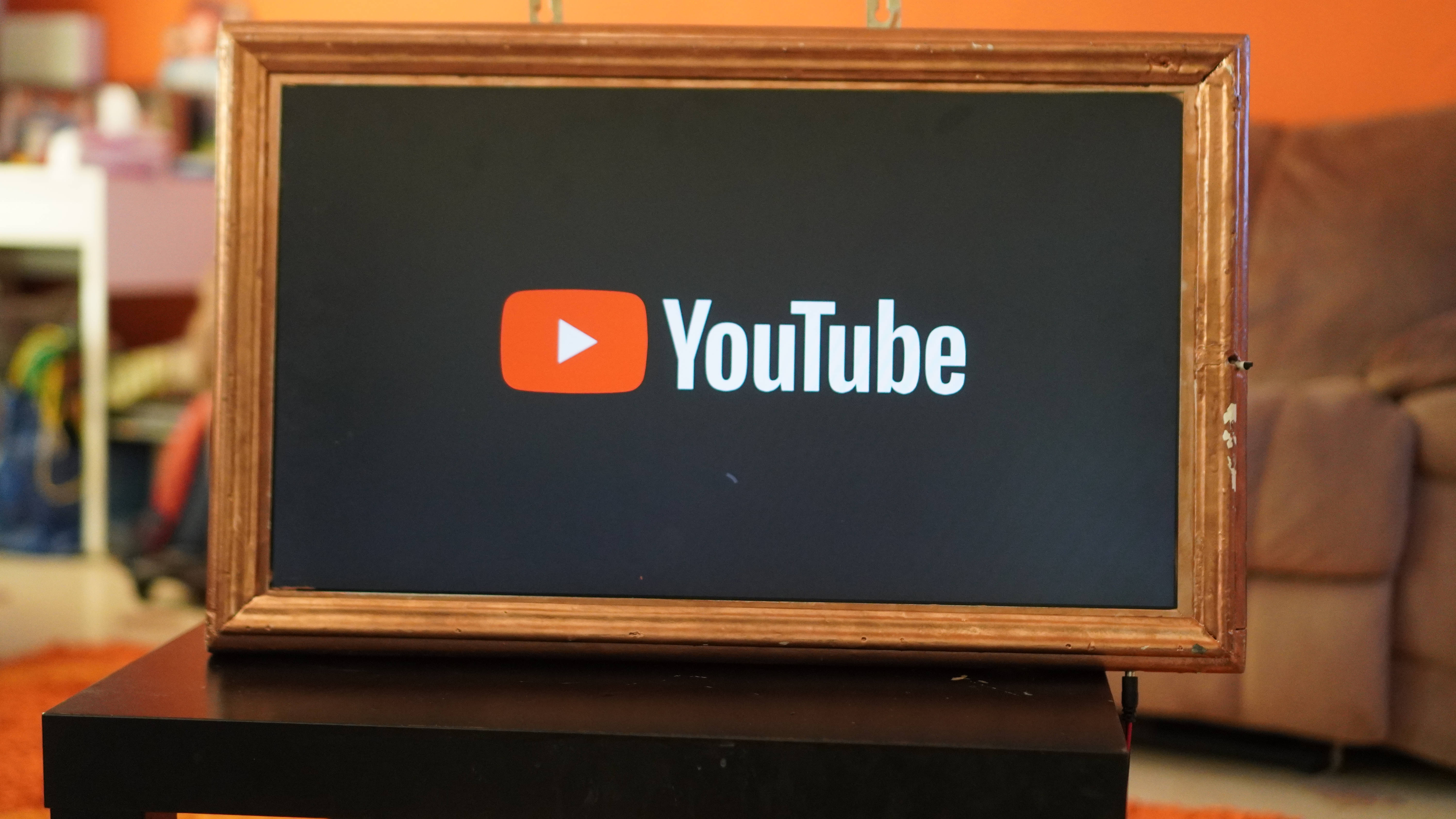 標誌 桌布 壁紙 — YouTube標誌顯示在一個螢幕中，螢幕鑲嵌在質樸的木框內，放置在溫暖照明的客廳中的一個深色支架上。