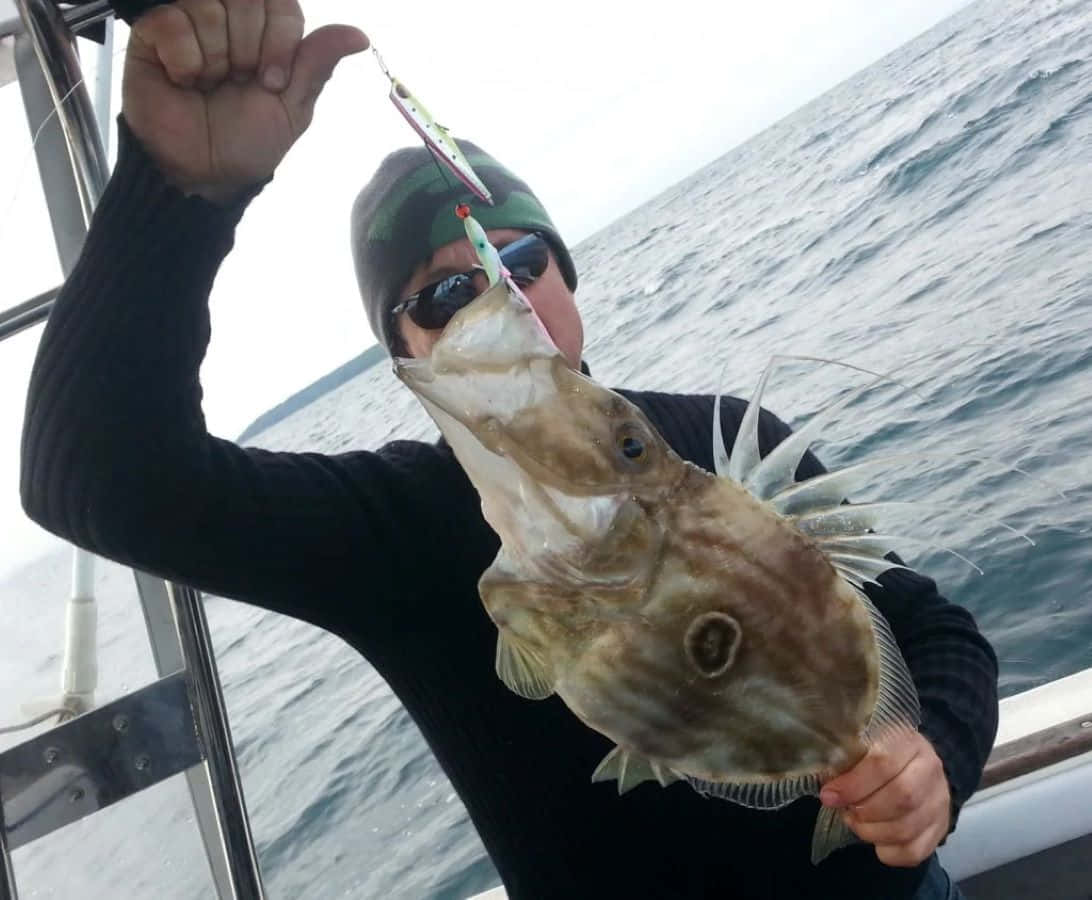  壁紙 — 一名漁夫在船上自豪地展示一條用彩色魚餌釣到的大魚，魚身佈滿尖刺，背景是波濤洶湧的大海。