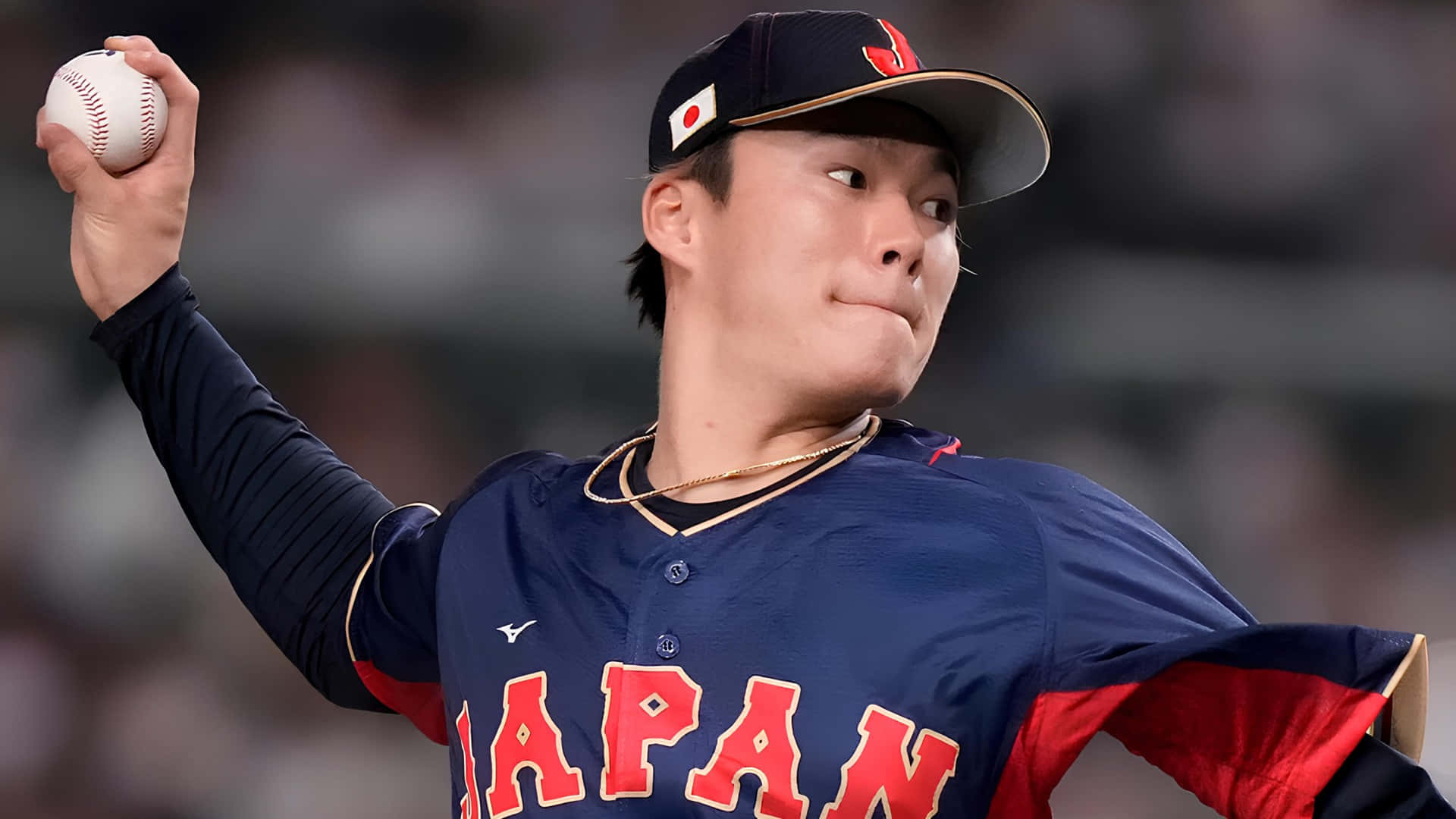  壁紙 — 一位身穿海軍藍和紅色制服嘅日本棒球投手喺夜間比賽中準備投球。