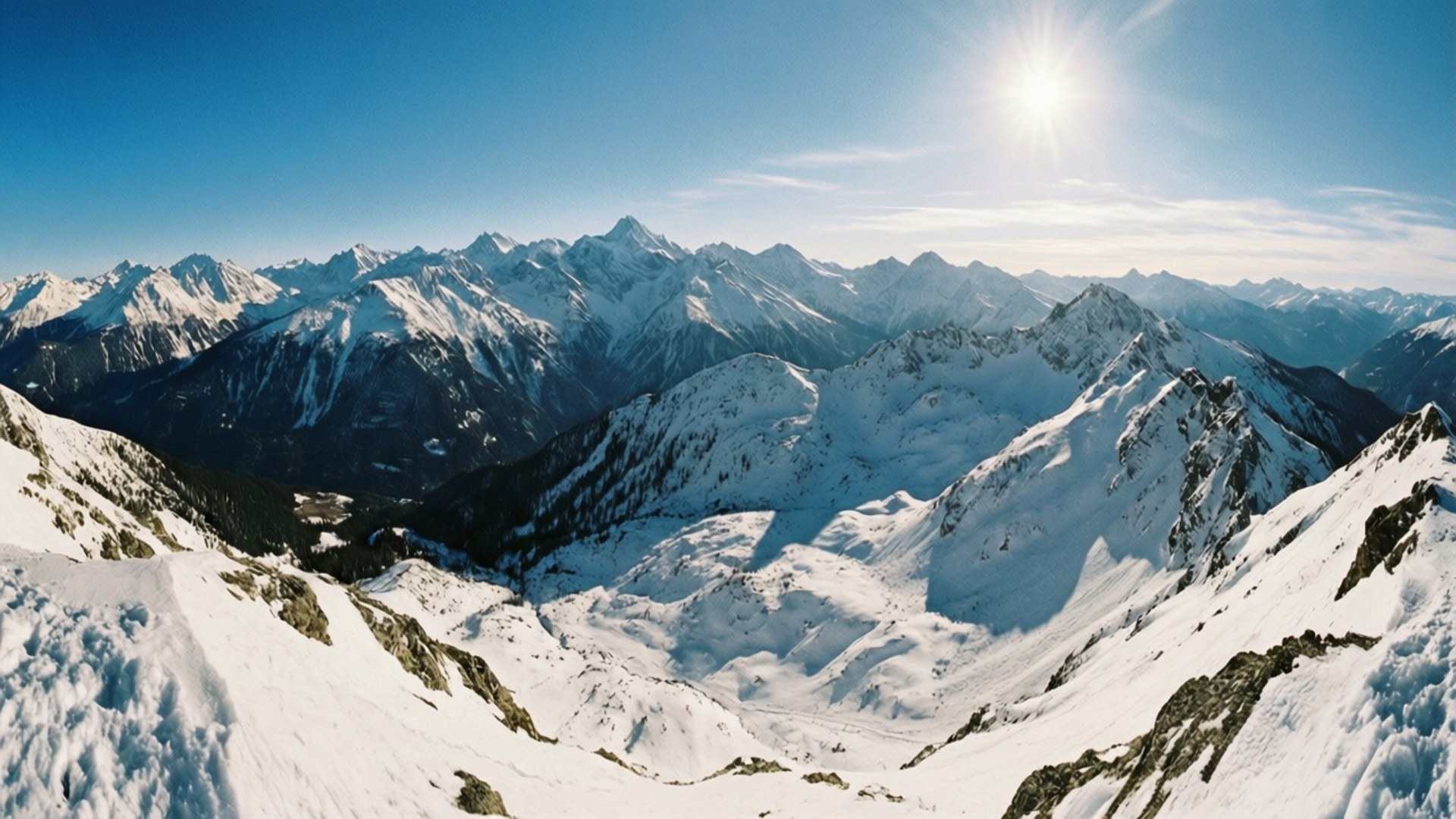Snowy Mountain Panorama 壁紙 — 在燦爛陽光和清澈藍天下，白雪覆蓋的山峰令人嘆為觀止的全景。