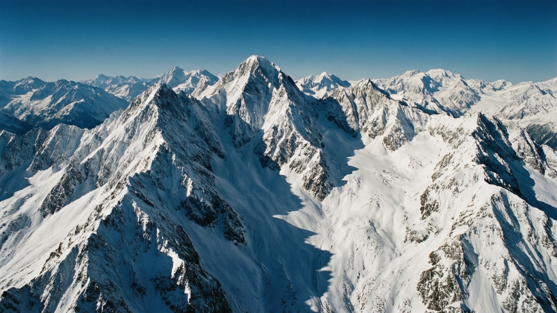 Aerial Mountain Range 壁紙 — 在清澈深藍的天空下，鋸齒狀積雪山峰的鳥瞰圖。