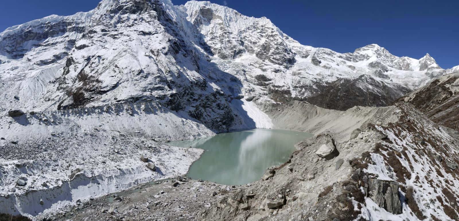  壁紙 — 在晴朗的藍天下，一個原始碧綠的冰川湖坐落於崎嶇的雪山山谷中。