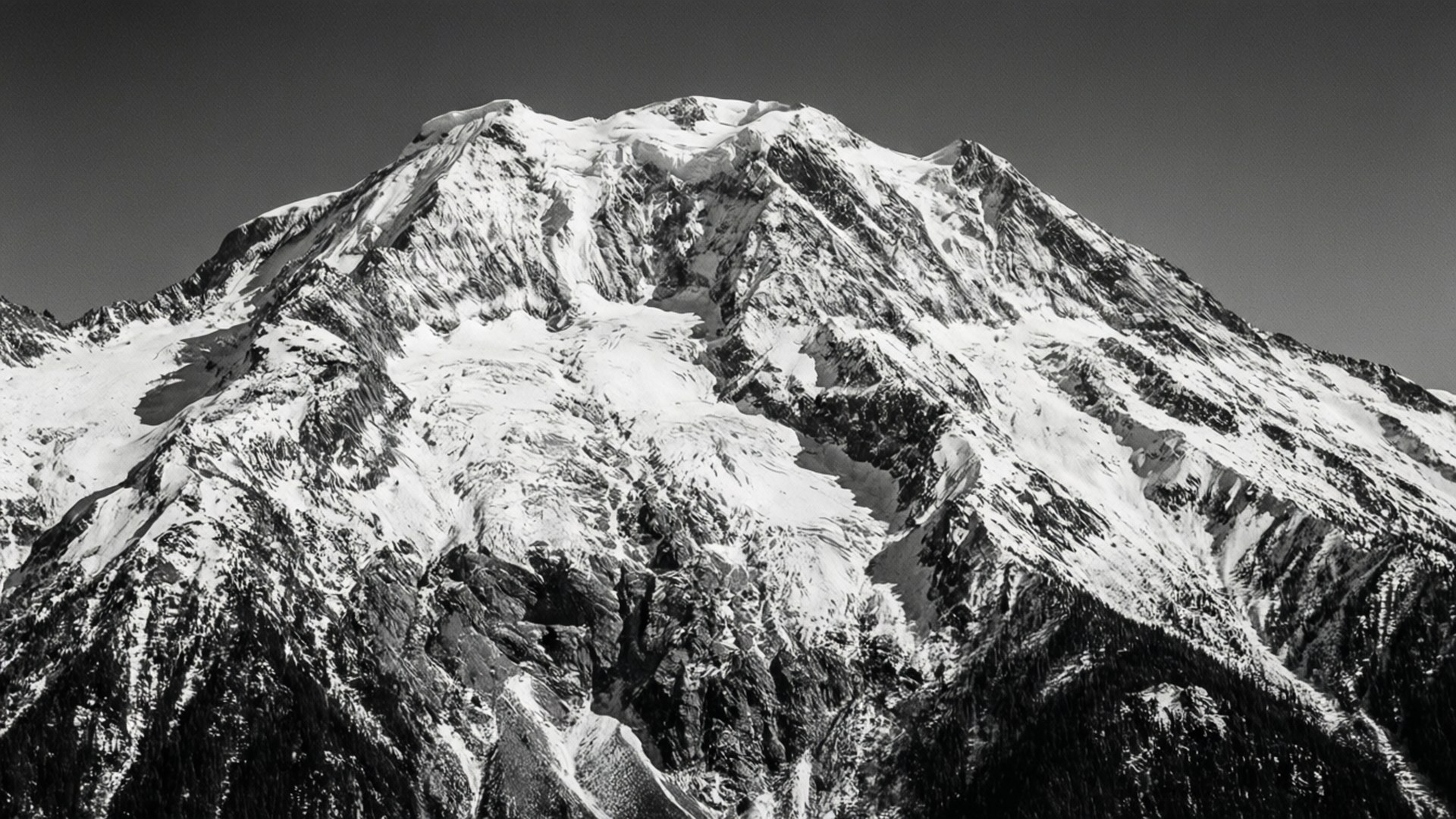 Monochrome Mountain 壁紙 — 在晴朗的天空下，一個黑白分明的山峰，冰雪依附在鋸齒狀的山脊上。