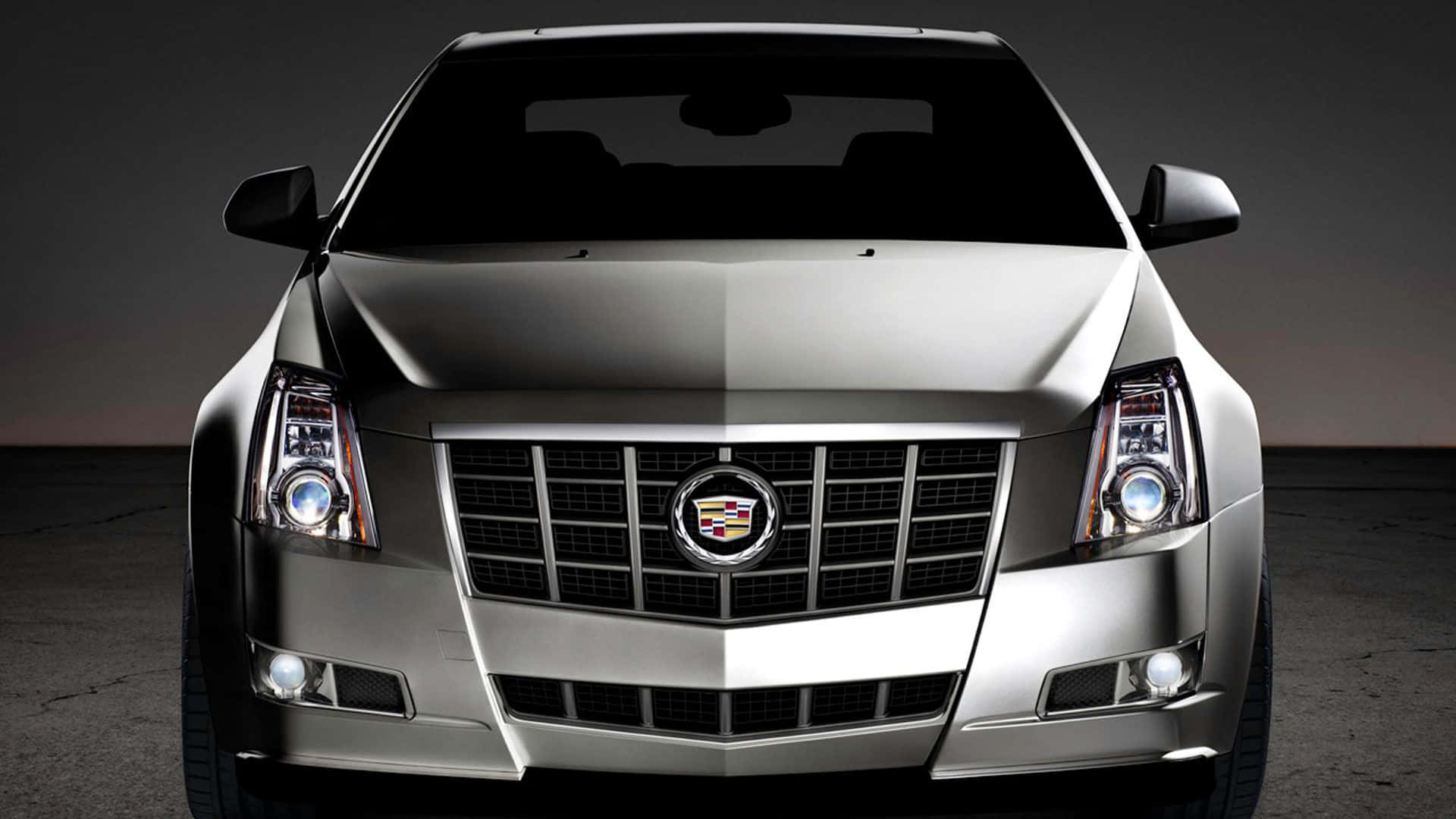 Cadillac Cts 桌布 壁紙 — 在深色工作室背景下，一輛時尚銀色凱迪拉克的前視圖，車頭燈發光。