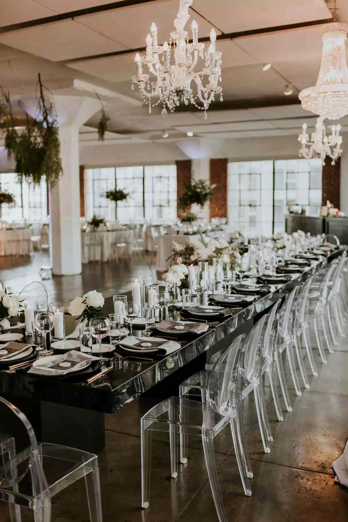 Black And White Wedding 桌布 壁紙 — 在現代工業風大廳的水晶吊燈下，一張長長的黑色餐桌擺放著白色鮮花和玻璃器皿。