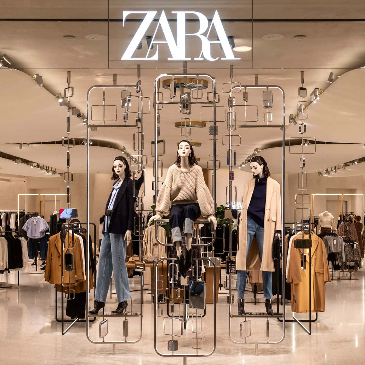 Zara 桌布 壁紙 — Zara 店內的三個人體模型在幾何金屬框架和溫暖燈光下展示秋季時裝。