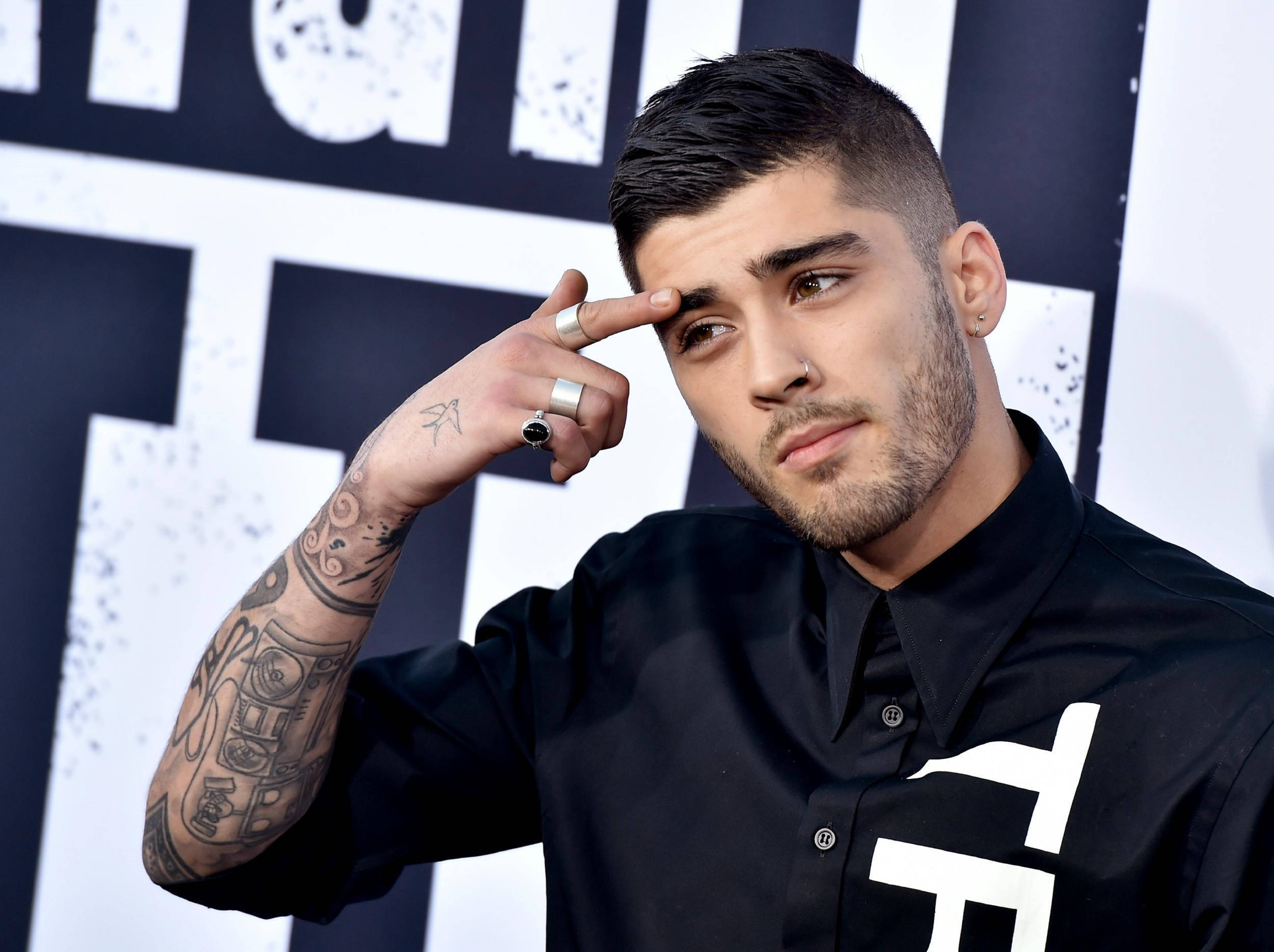 zayn 桌布 壁紙 — Zayn Malik 將手指放在太陽穴，身穿黑色襯衫和戒指，在醒目的黑白圖形背景前擺姿勢。