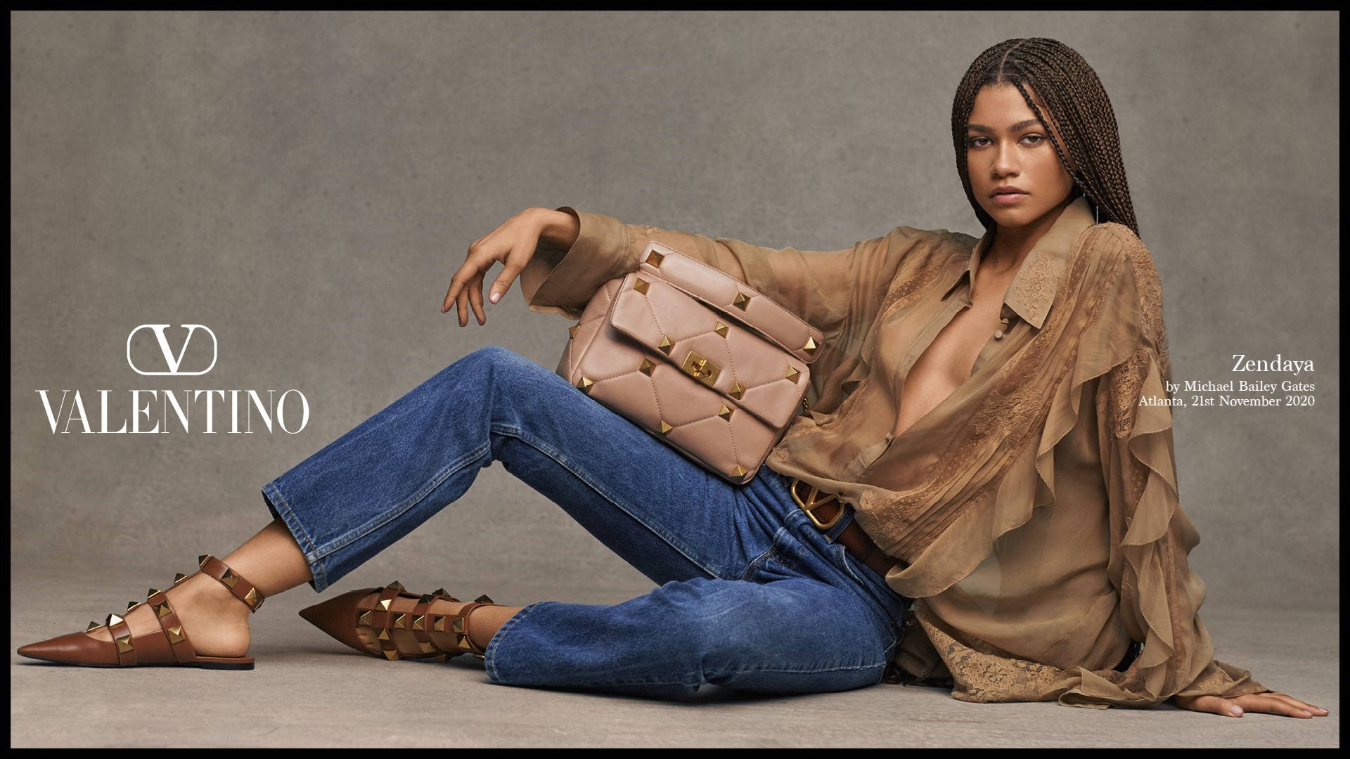 Celebrity 桌布 壁紙 — Zendaya 在Valentino廣告中自信地擺姿勢，身穿米色襯衫、藍色牛仔褲和鉚釘飾品，背景為中性工作室背景。