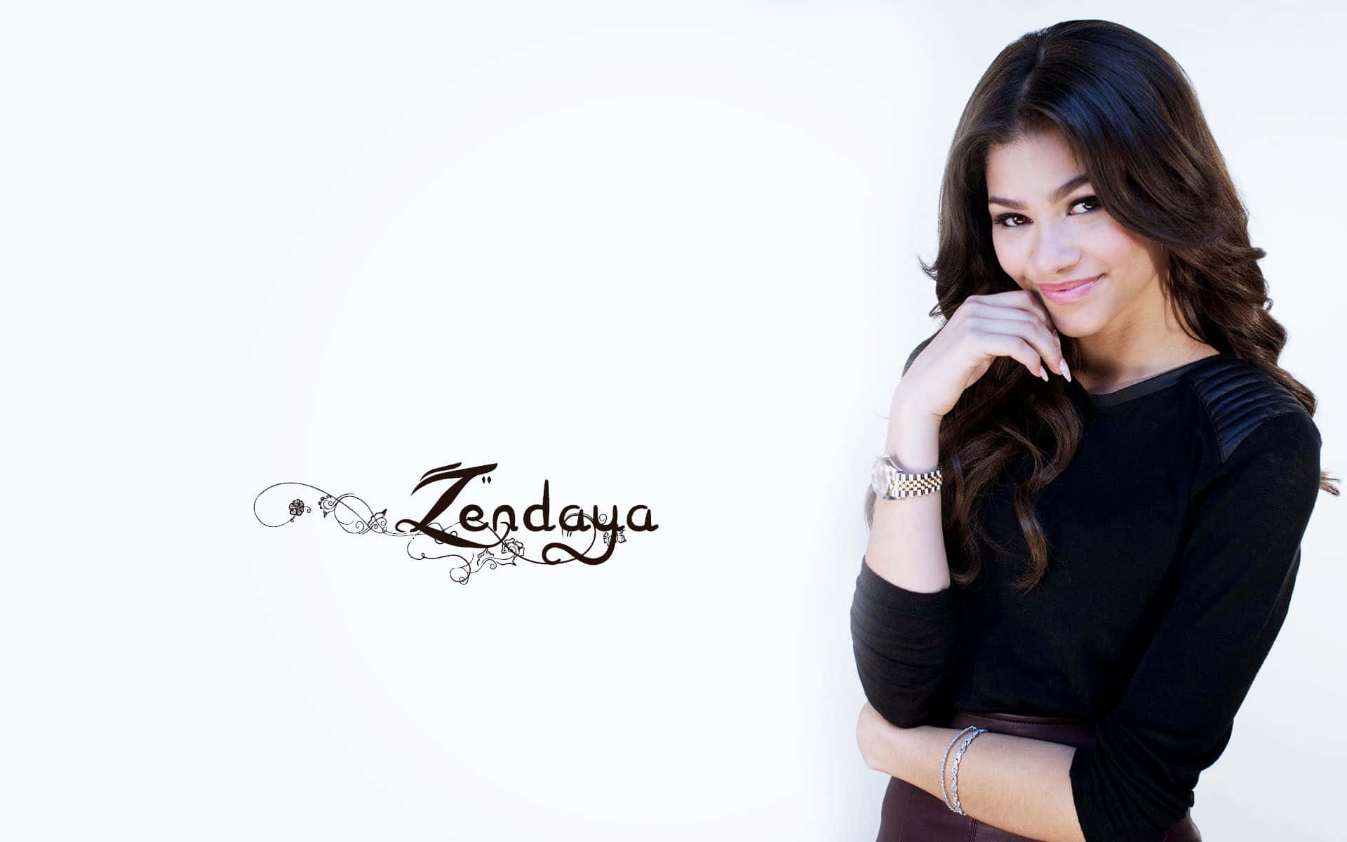 Celebrity 桌布 壁紙 — Zendaya 在乾淨的白色背景前擺出溫柔的笑容，她的深色捲髮框住她的臉，下巴擱在手上。