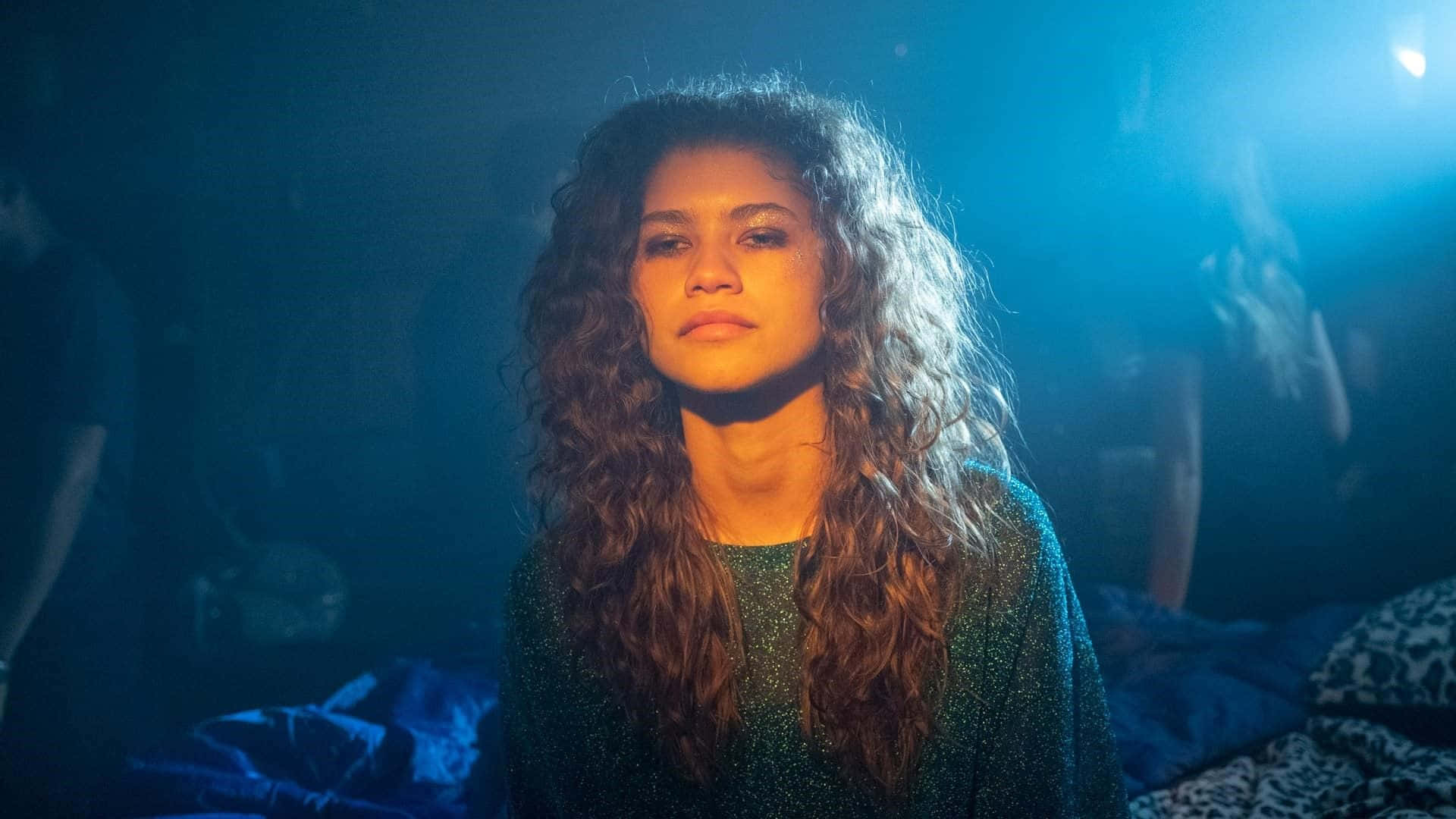 Euphoria Hbo iPhone 桌布 壁紙 — Zendaya 留著捲髮，在昏暗的演唱會場景中，於戲劇性的藍色舞台燈光下向前凝視。