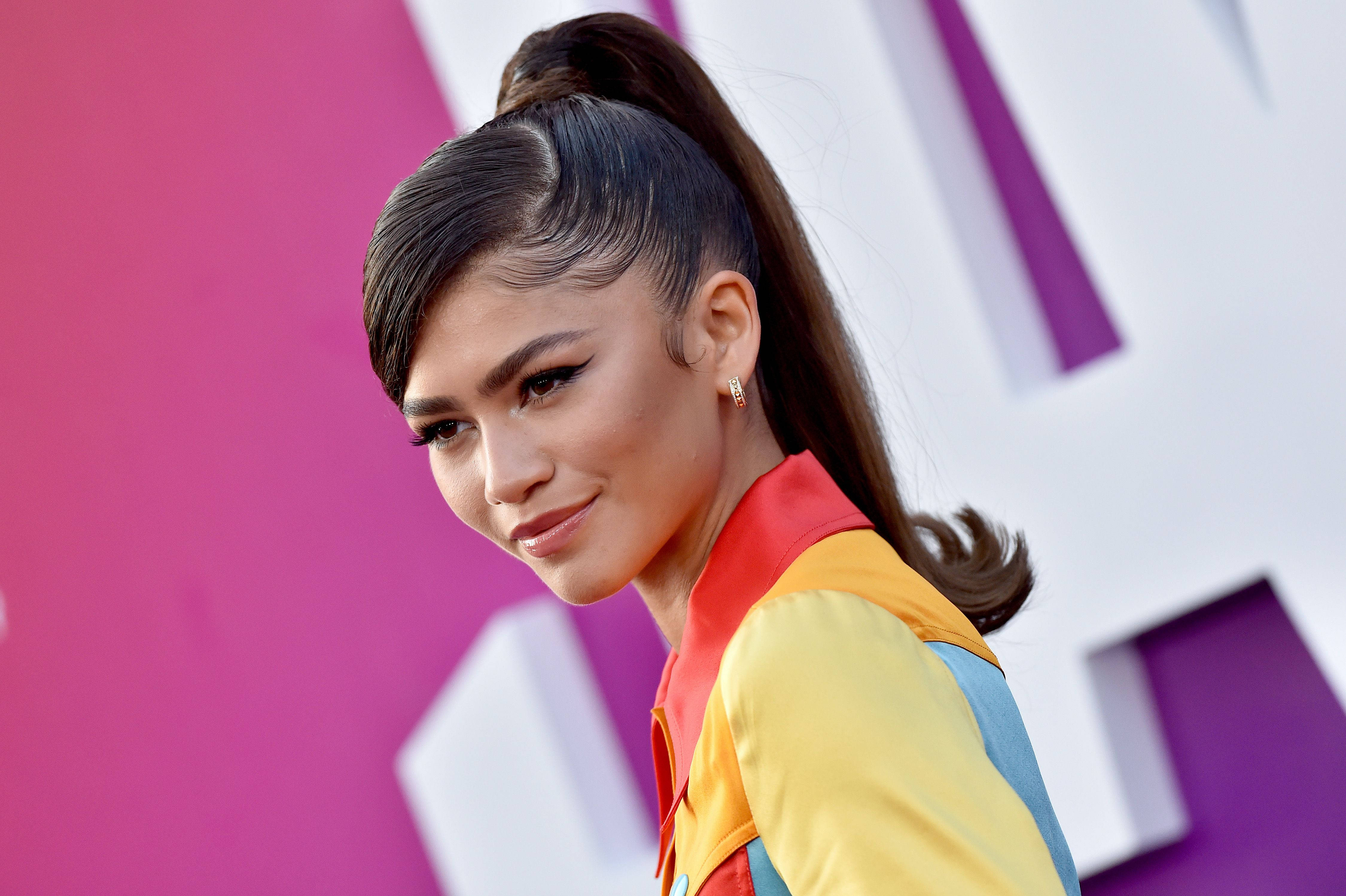 Zendaya 桌布 壁紙 — Zendaya 自信地擺姿勢，身穿鮮豔的色塊服裝，背景是大膽的粉紅和白色幾何圖案。