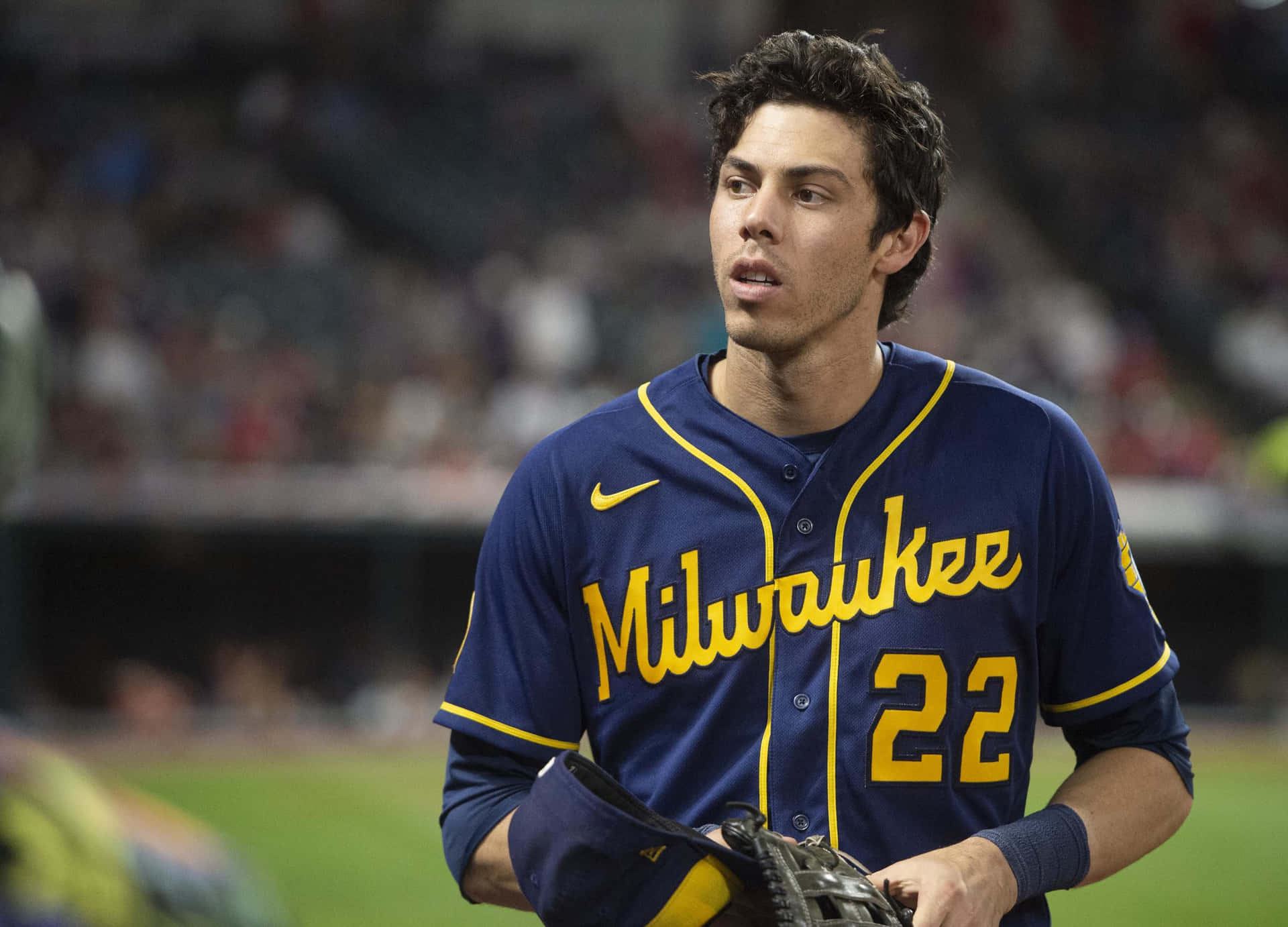 身穿密爾瓦基球衣的棒球運動員在夜間球場上拿著手套。 — MLB 壁紙