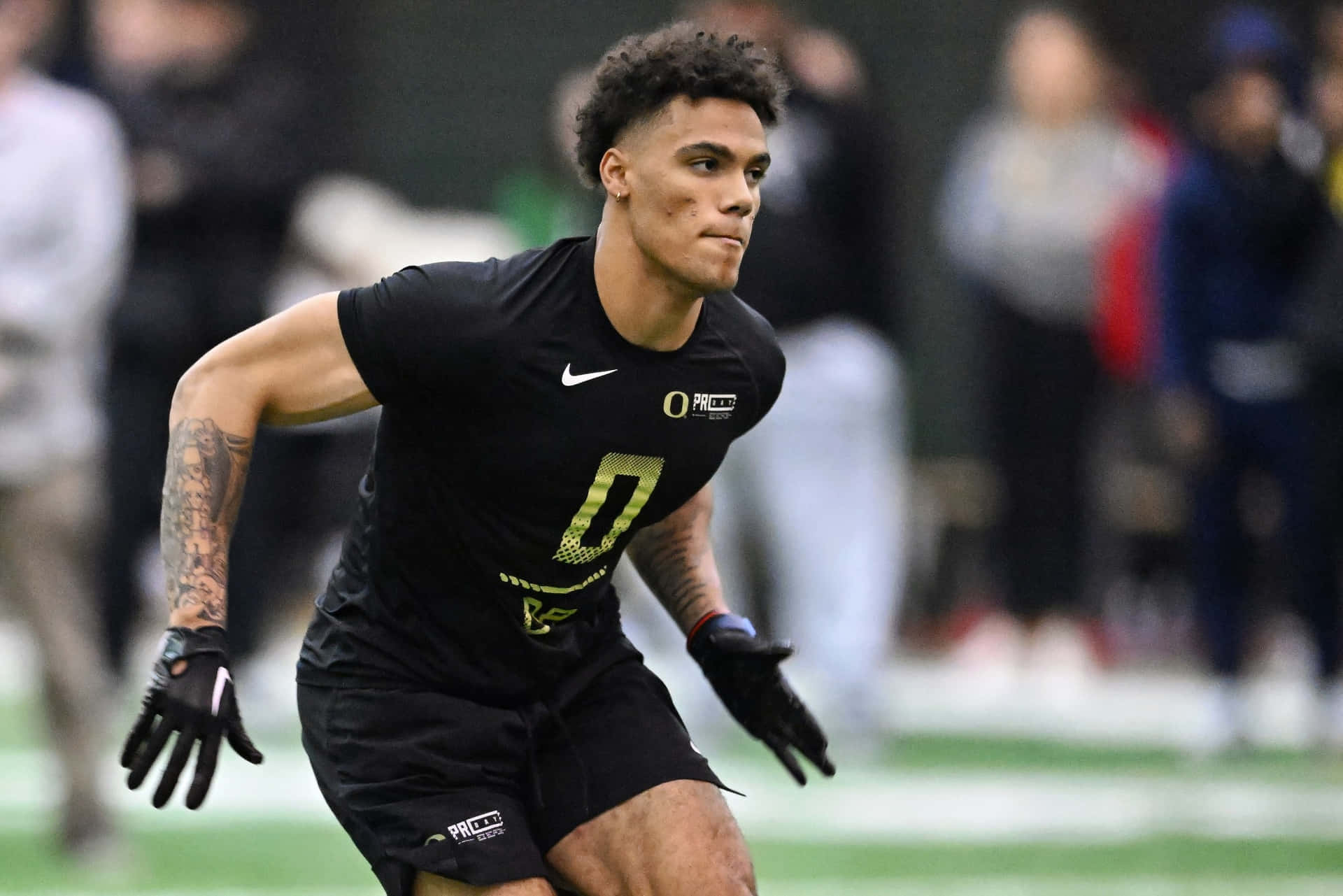  壁紙 — 一名專注的美式足球員身穿黑色和金色裝備，在綠色場地上衝刺，背景有模糊的觀眾。