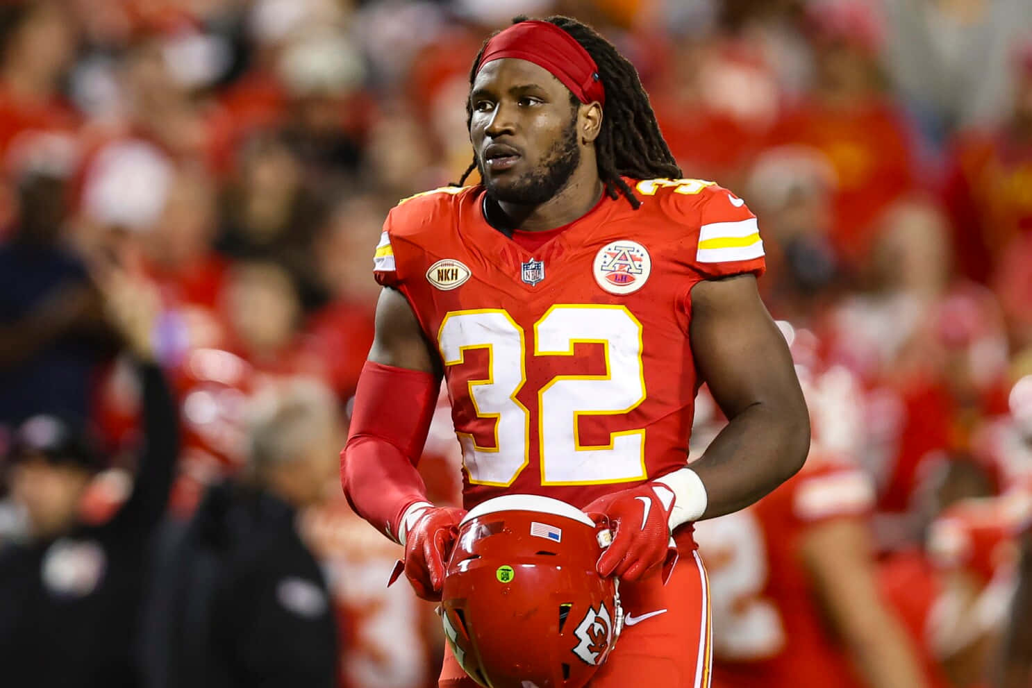  壁紙 — 一位專注的NFL球員身穿紅色32號球衣，在明亮燈光下於球場上行走時手持頭盔。