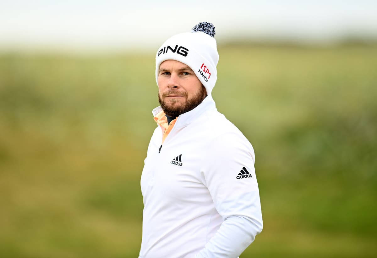 Tyrrell Hatton 桌布 壁紙 — 一位專注的高爾夫球手戴著白色毛帽和外套，站在有模糊自然背景的草地上。