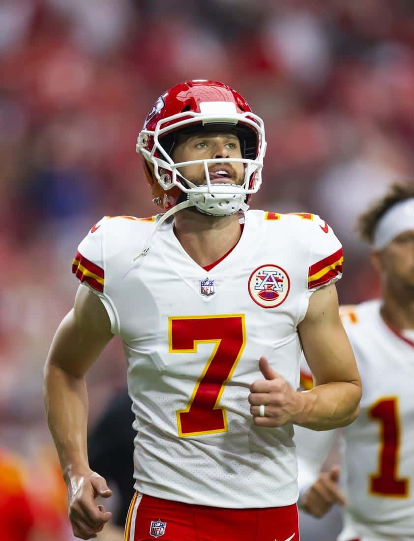  壁紙 — 一位專注的NFL四分衛身穿白色和紅色7號球衣，在球場燈光下比賽時豎起大拇指。