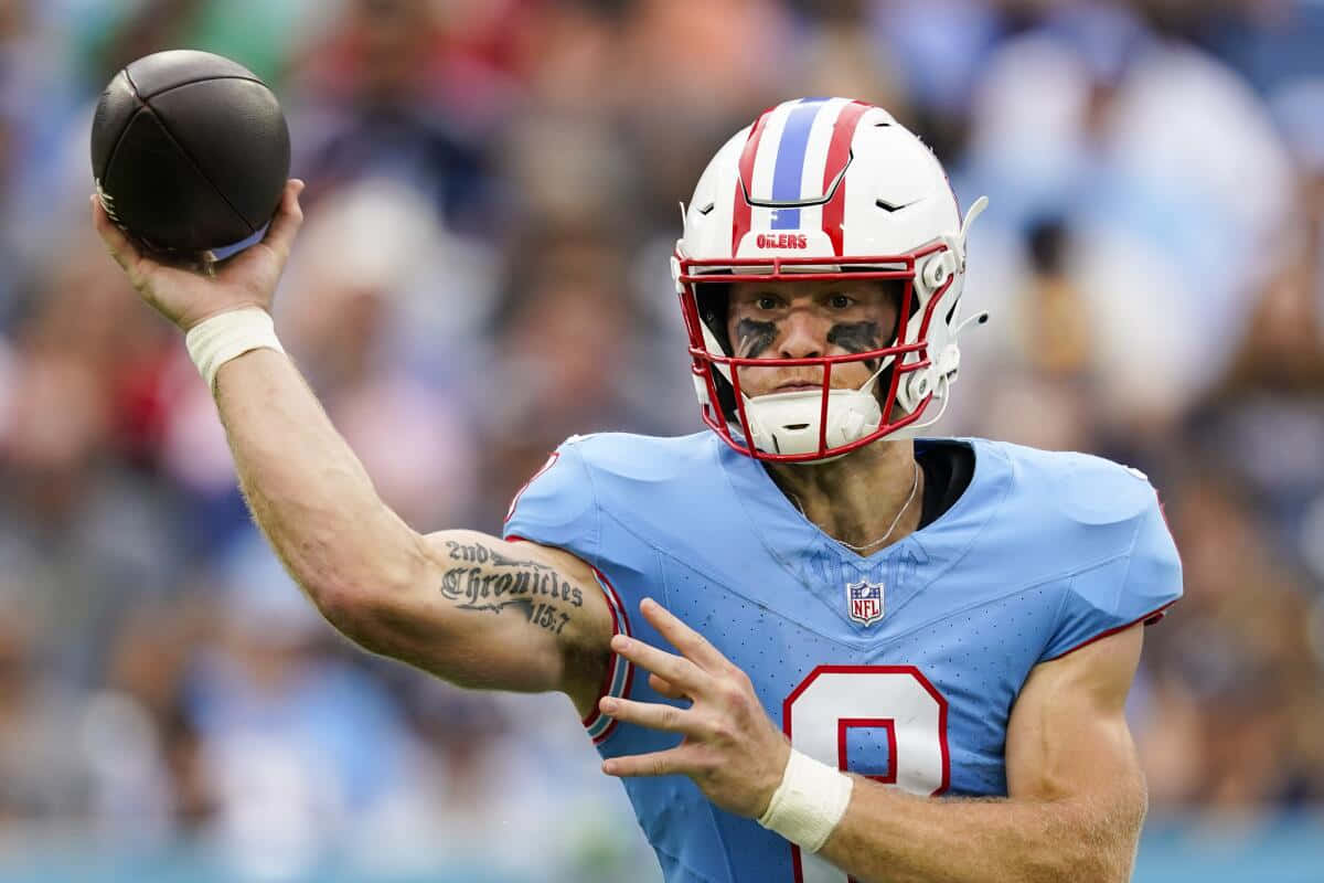  壁紙 — 一位專注的NFL四分衛，身穿淺藍色8號球衣，在日間比賽中揮臂準備傳球。