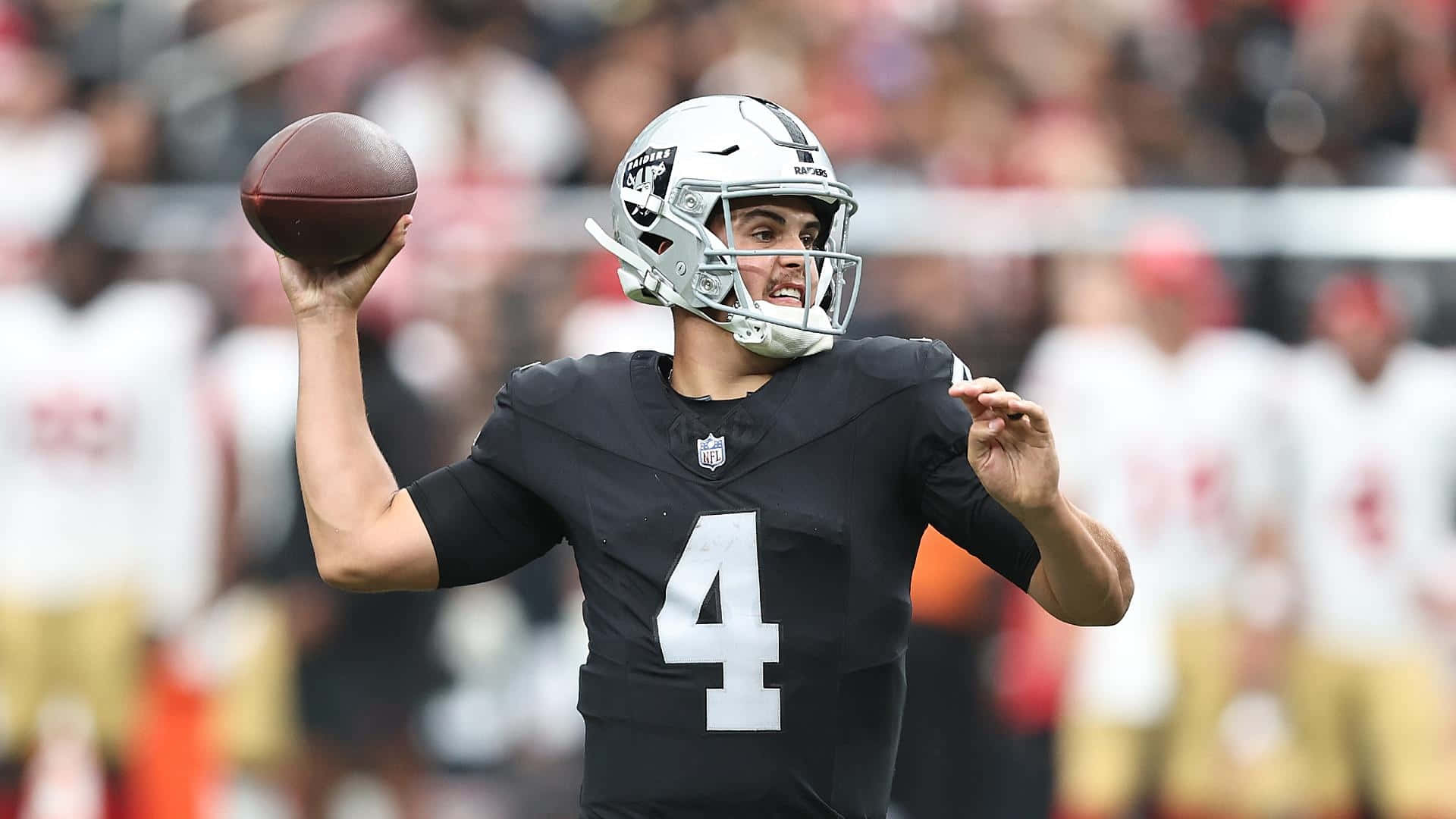  壁紙 — 一位專注的NFL四分衛身穿黑色球衣，背號四號，在日間比賽中揮臂準備傳球。