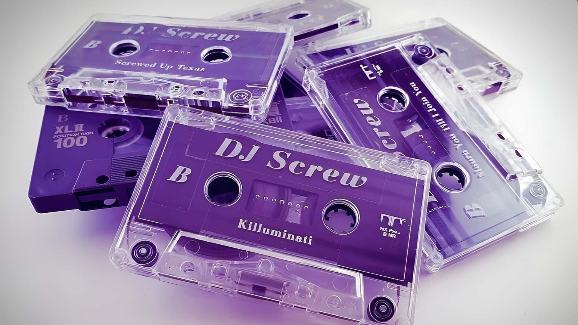 壁紙 — 紫色卡式帶疊起，帶有DJ Screw標籤，在柔和燈光下於白色表面發光。