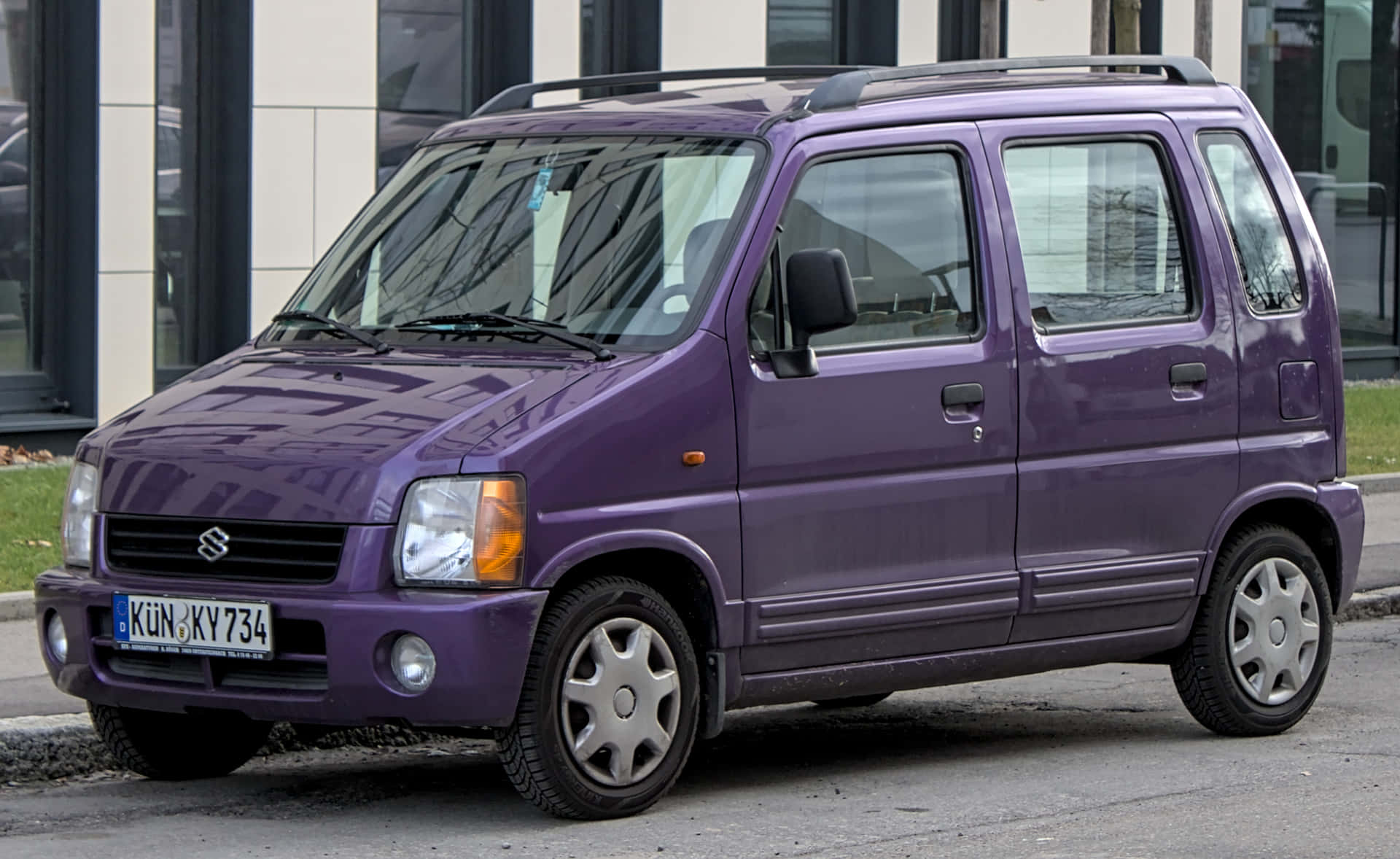  壁紙 — 一輛充滿活力的紫色鈴木Every小型貨車停放在城市街道上，背景是現代建築。