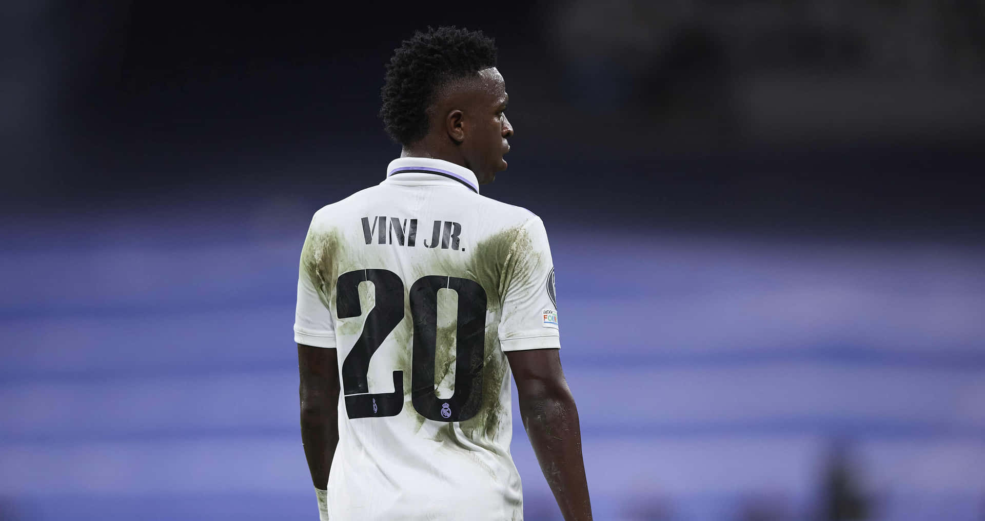  壁紙 — 一名身穿白色球衣、印有「VINI JR」和20號的足球員背對鏡頭，站在模糊的球場上。
