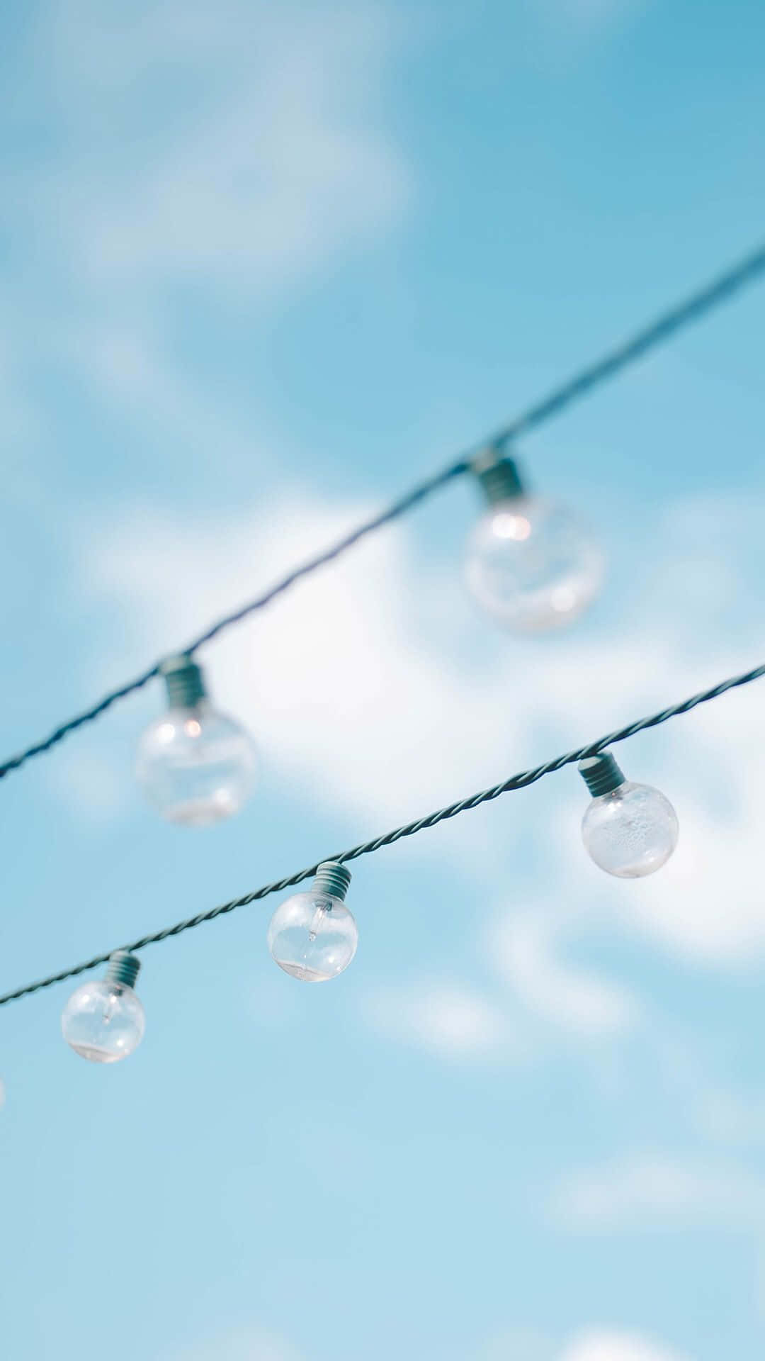 Blue Sky Aesthetic 桌布 壁紙 — 一串串燈飾懸掛在柔和藍天與蓬鬆白雲之間，營造寧靜的戶外氛圍。