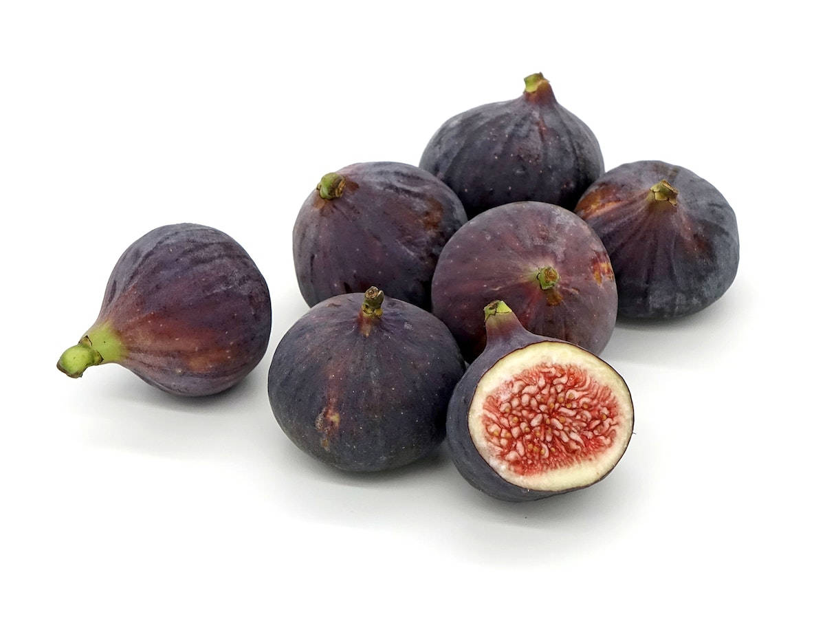 Fruit 桌布 壁紙 — 一串成熟的紫色無花果，其中一個切開一半，露出粉紅色果肉和種子，背景為純白色。