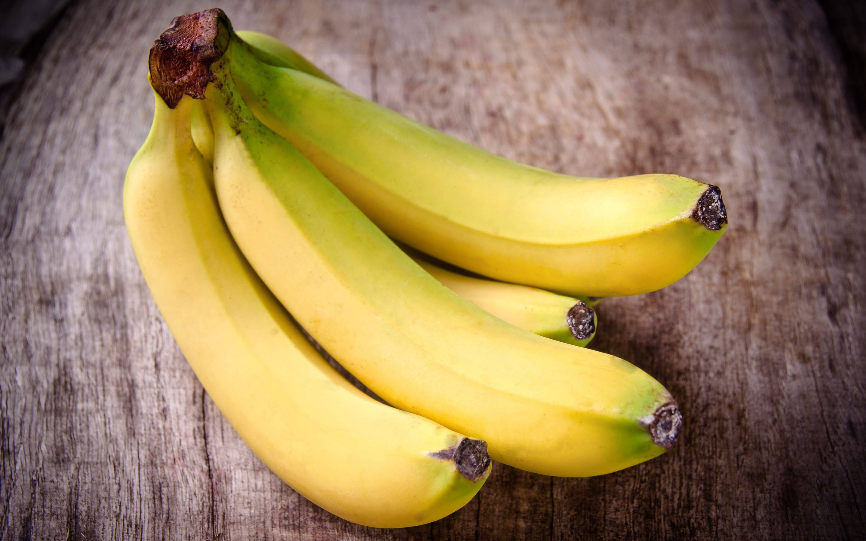 Plantain 桌布 壁紙 — 一串成熟的黃色香蕉，帶有綠色尖端，放在經風化的木質表面上。