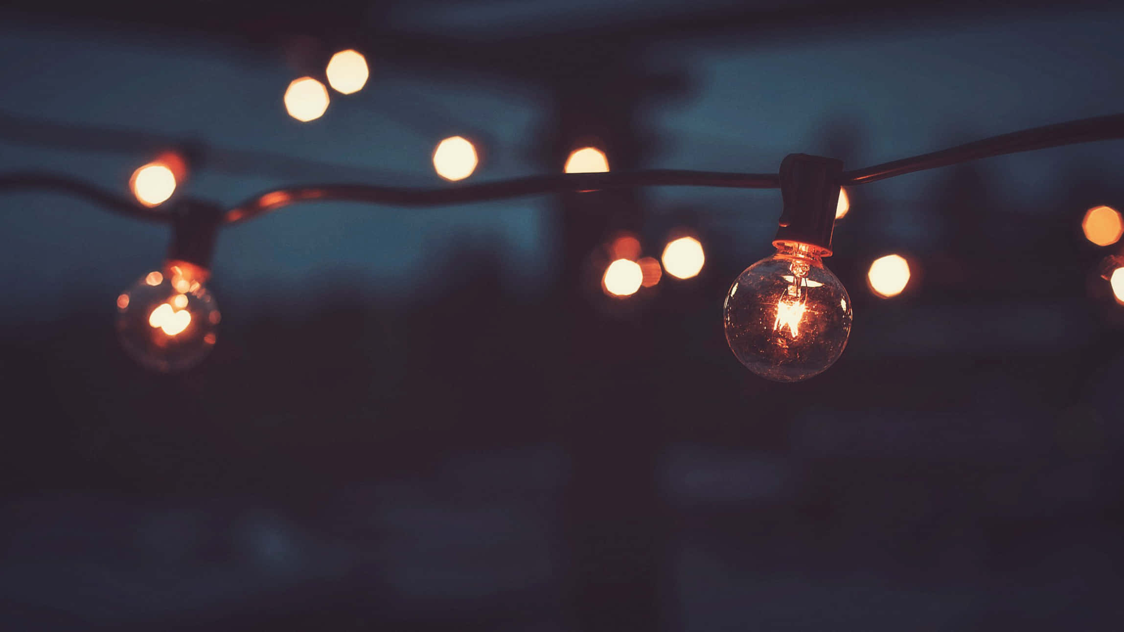 Light 桌布 壁紙 — 一串發光的復古燈泡懸掛在昏暗的暮色天空中，營造出溫暖的散景效果。