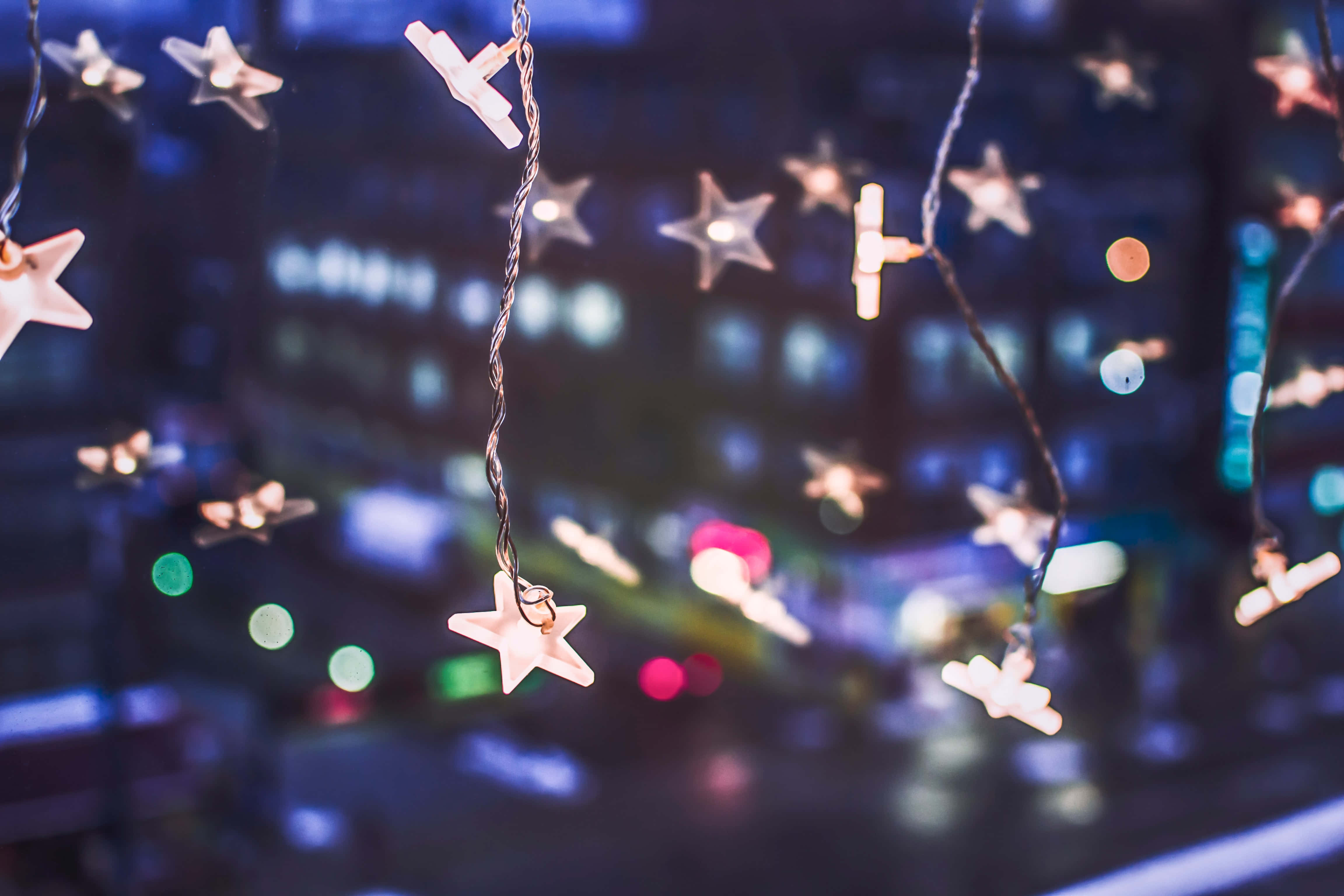 Christmas Light 桌布 壁紙 — 一串發光的星形燈飾在柔焦中懸掛，背景是模糊的城市夜景。
