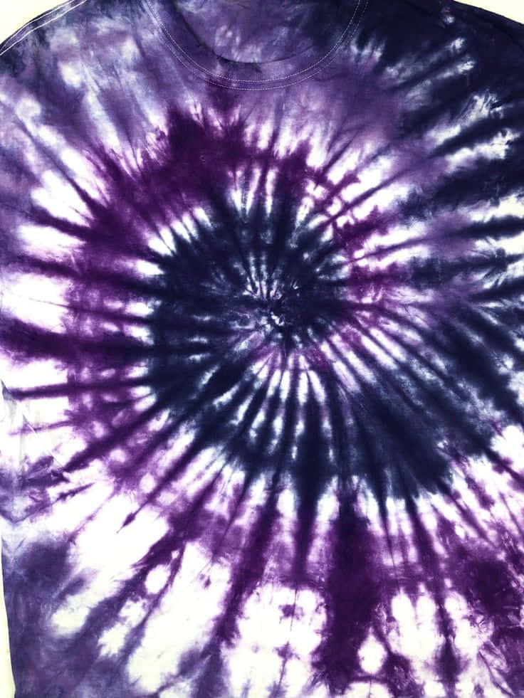 Purple Dye 桌布 壁紙 — 一件T恤的近距离特写，带有从中心放射出的鲜艳紫色和白色螺旋扎染图案。