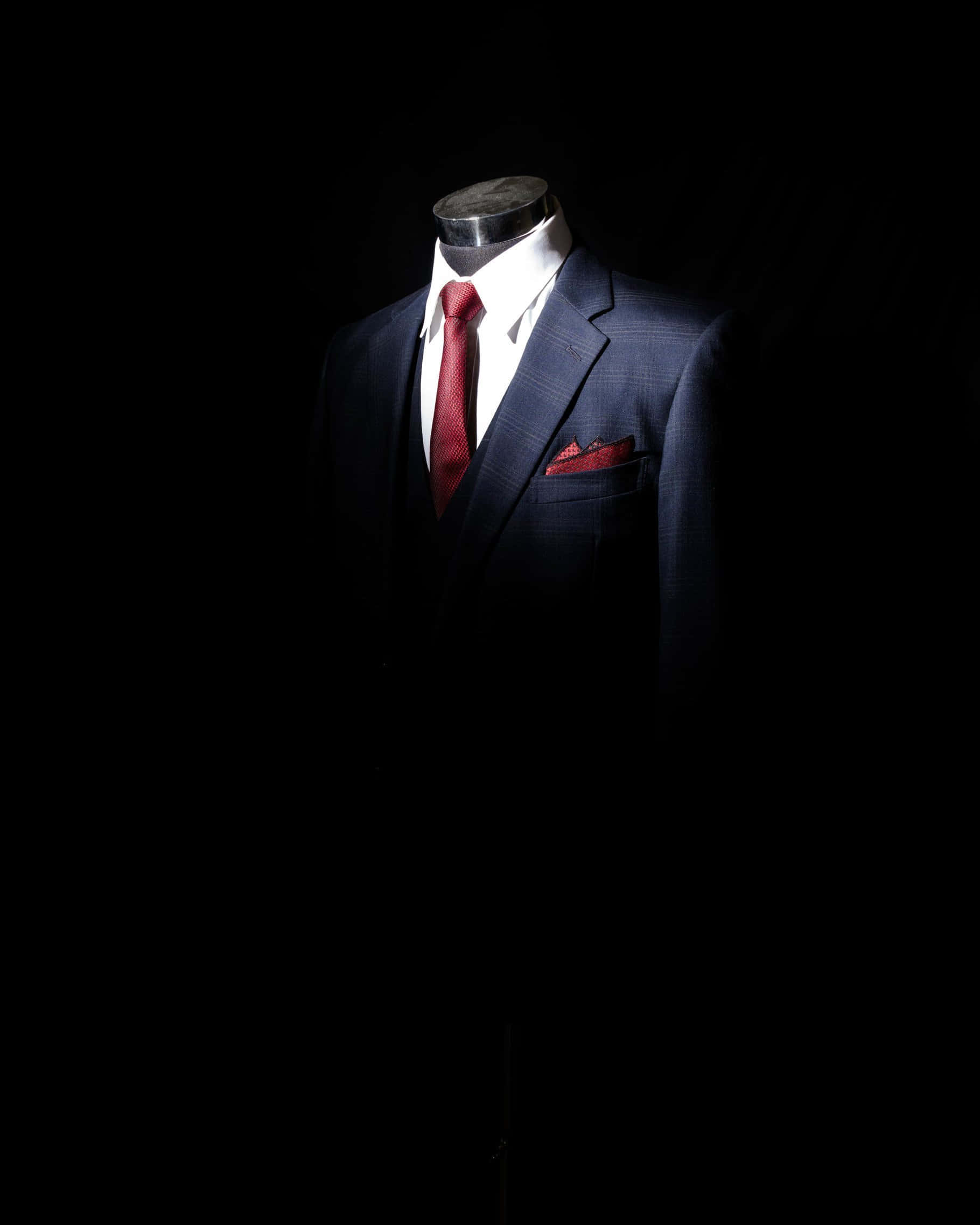 Red Tie 桌布 壁紙 — 一件剪裁俐落的海軍藍西裝，搭配紅色領帶和口袋方巾，在純黑背景上的戲劇性聚光燈下閃耀。