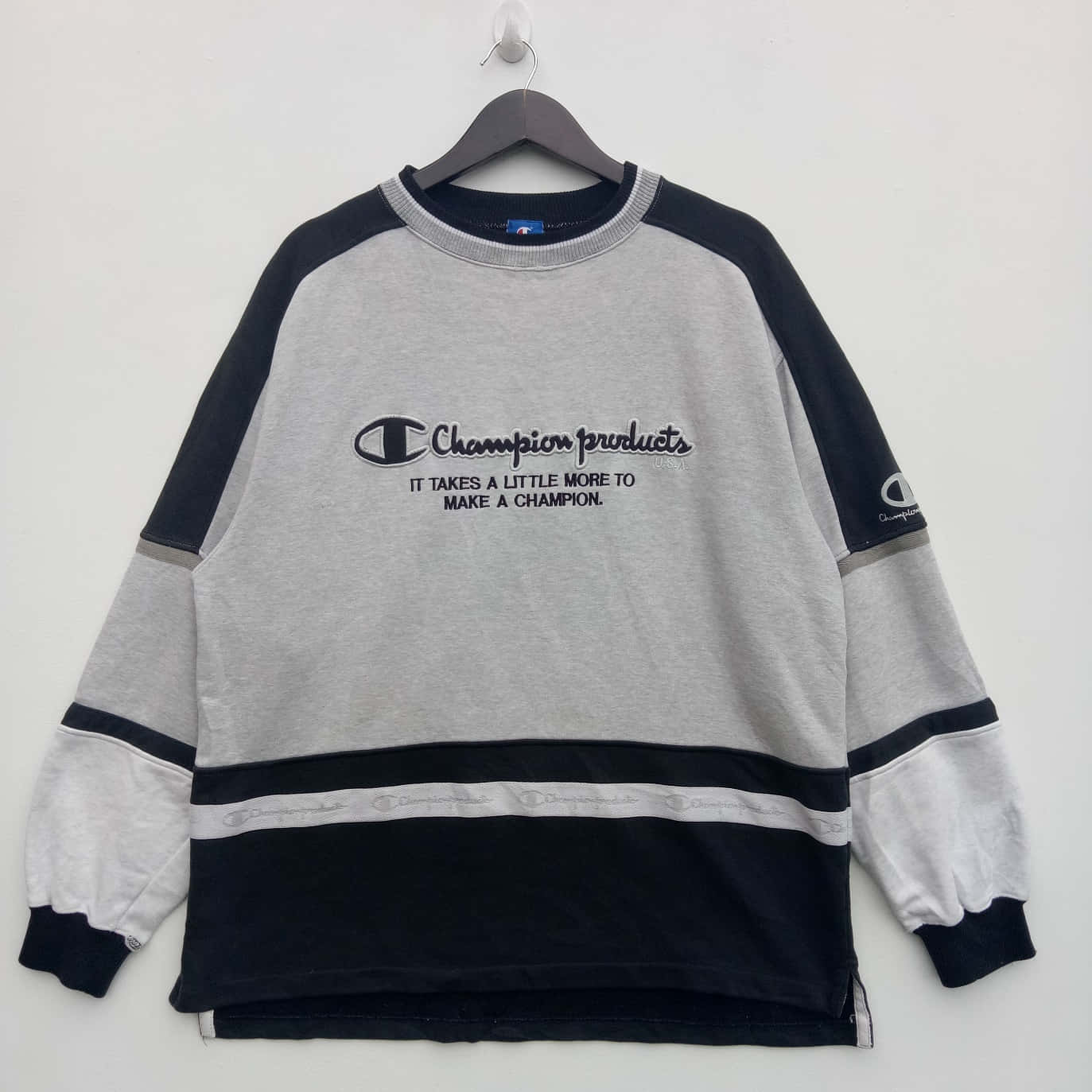Champion 桌布 壁紙 — 一件復古Champion衛衣，灰色衣身、黑色袖子、白色飾邊，掛在木衣架上，背景是純白牆壁。
