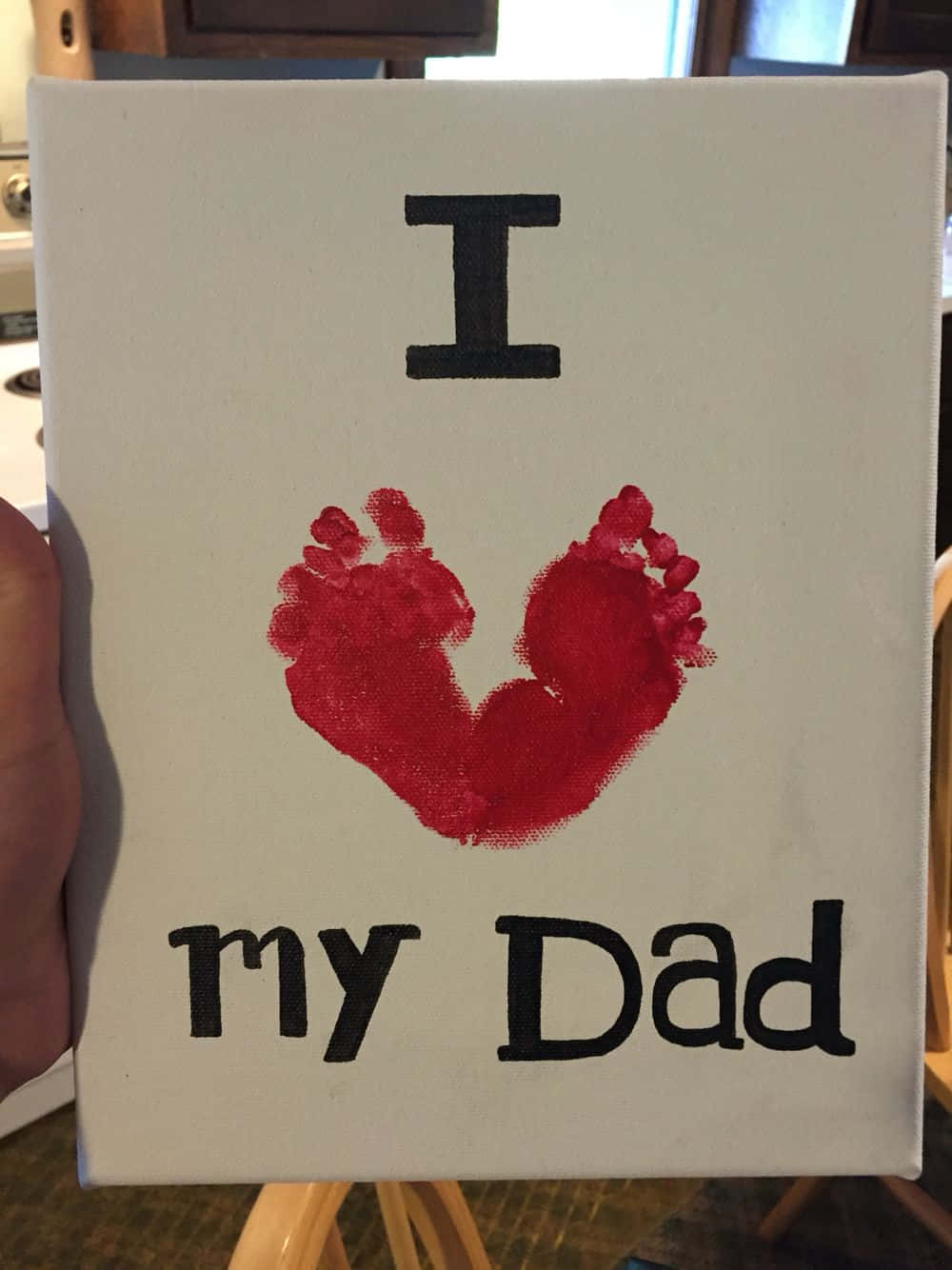 Fathers Day 桌布 壁紙 — 一件手工製作的帆布藝術品展示了兩個紅色嬰兒腳印形成一個心形，並有黑色字母寫著「I love my Dad」。