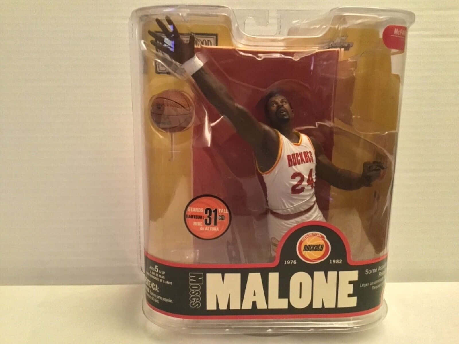 Man 桌布 壁紙 — 一件收藏級 Hakeem Olajuwon 可動人偶，身穿休士頓火箭球衣，正在灌籃，密封在透明塑膠包裝中，帶有紅黑品牌標誌。