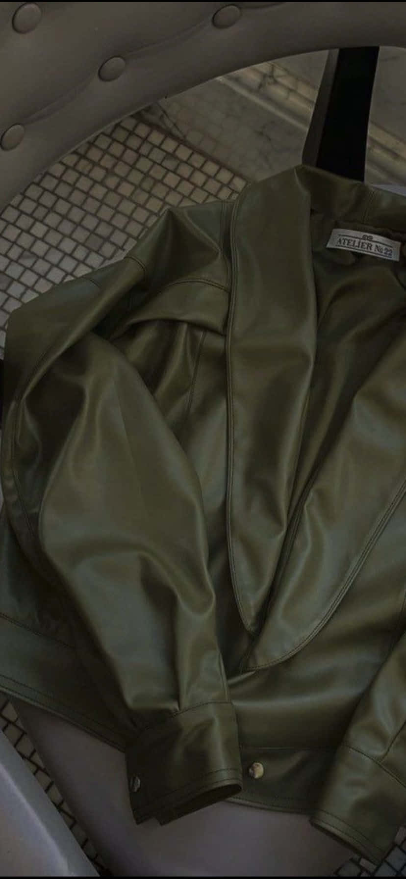 Olive Green iPhone 桌布 壁紙 — 一件橄欖綠色皮夾克搭在一張簇絨椅上，下方是瓷磚地板。