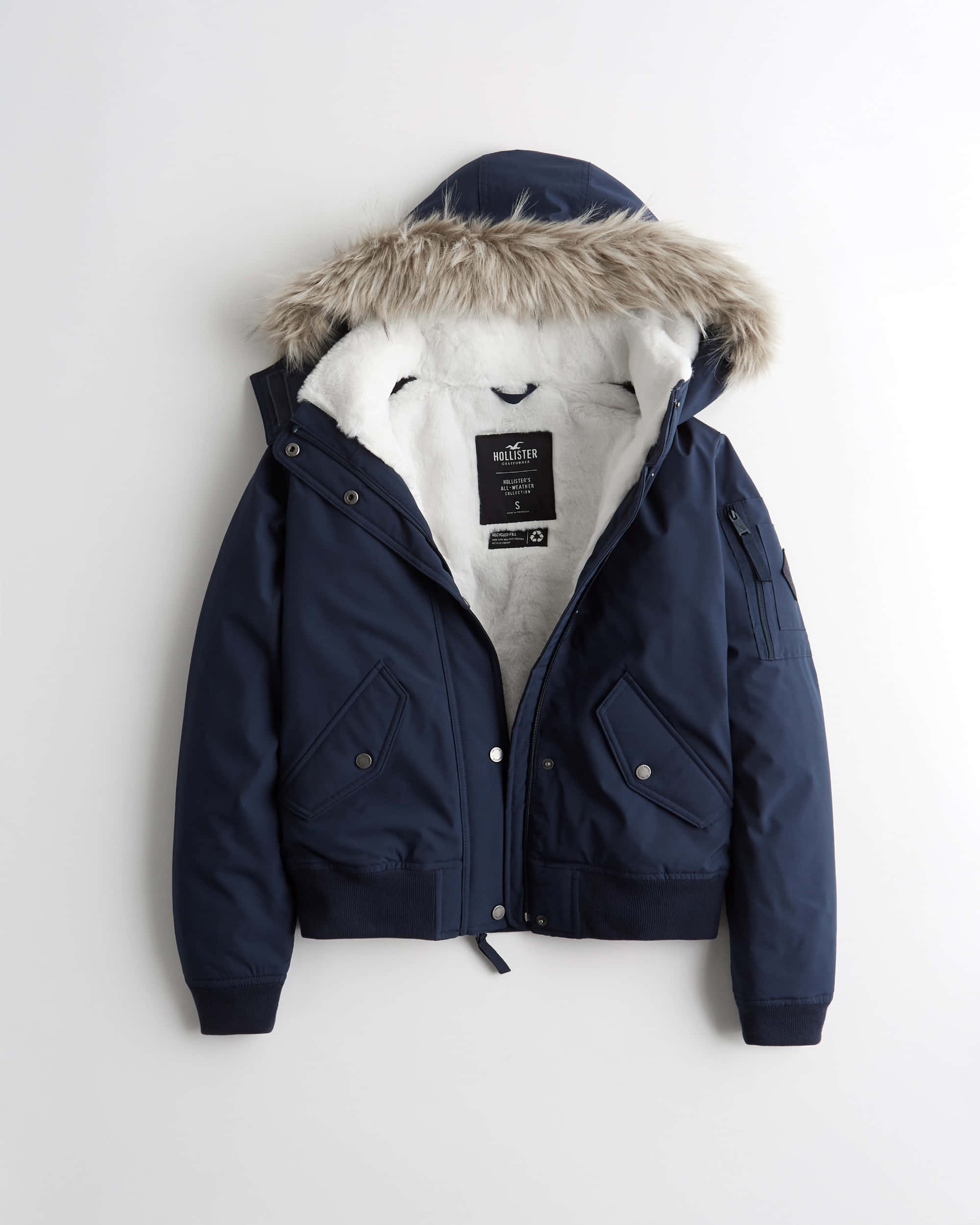 Hollister 桌布 壁紙 — 一件海軍藍色冬季外套，配有毛絨襯裡帽子和白色抓絨內襯，展示在純白色背景上。