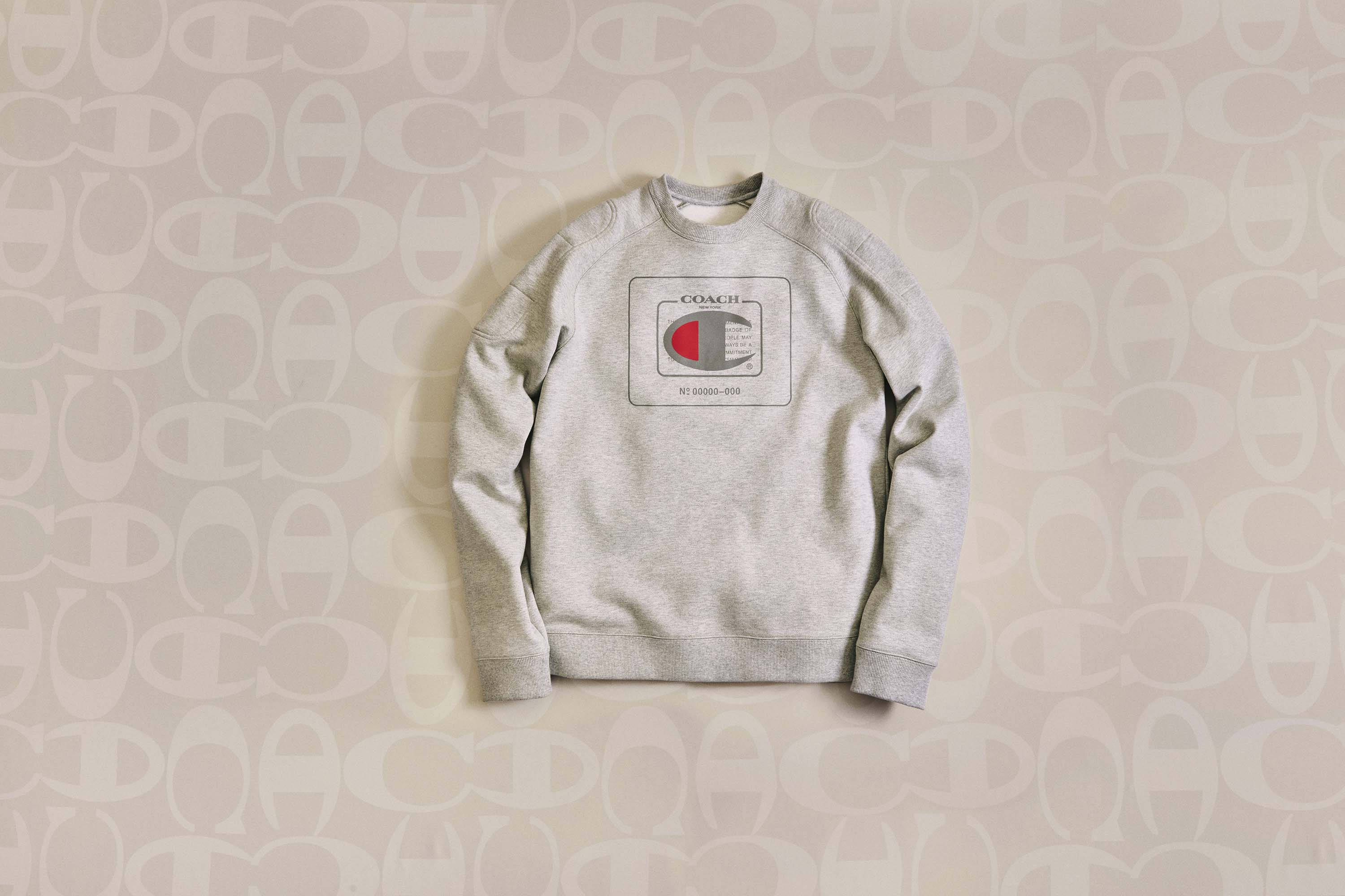 Champion 桌布 壁紙 — 一件灰色Champion連帽衫，帶有紅、白、藍色標誌，平放在重複的米色和白色C標誌壁紙背景上。