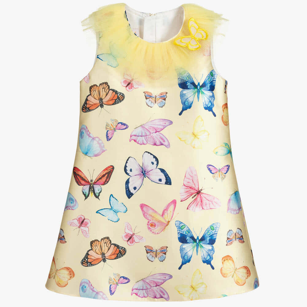Butterfly Dress 桌布 壁紙 — 一件無袖兒童連衣裙，帶有黃色薄紗領和奶油色背景上的彩色蝴蝶圖案。