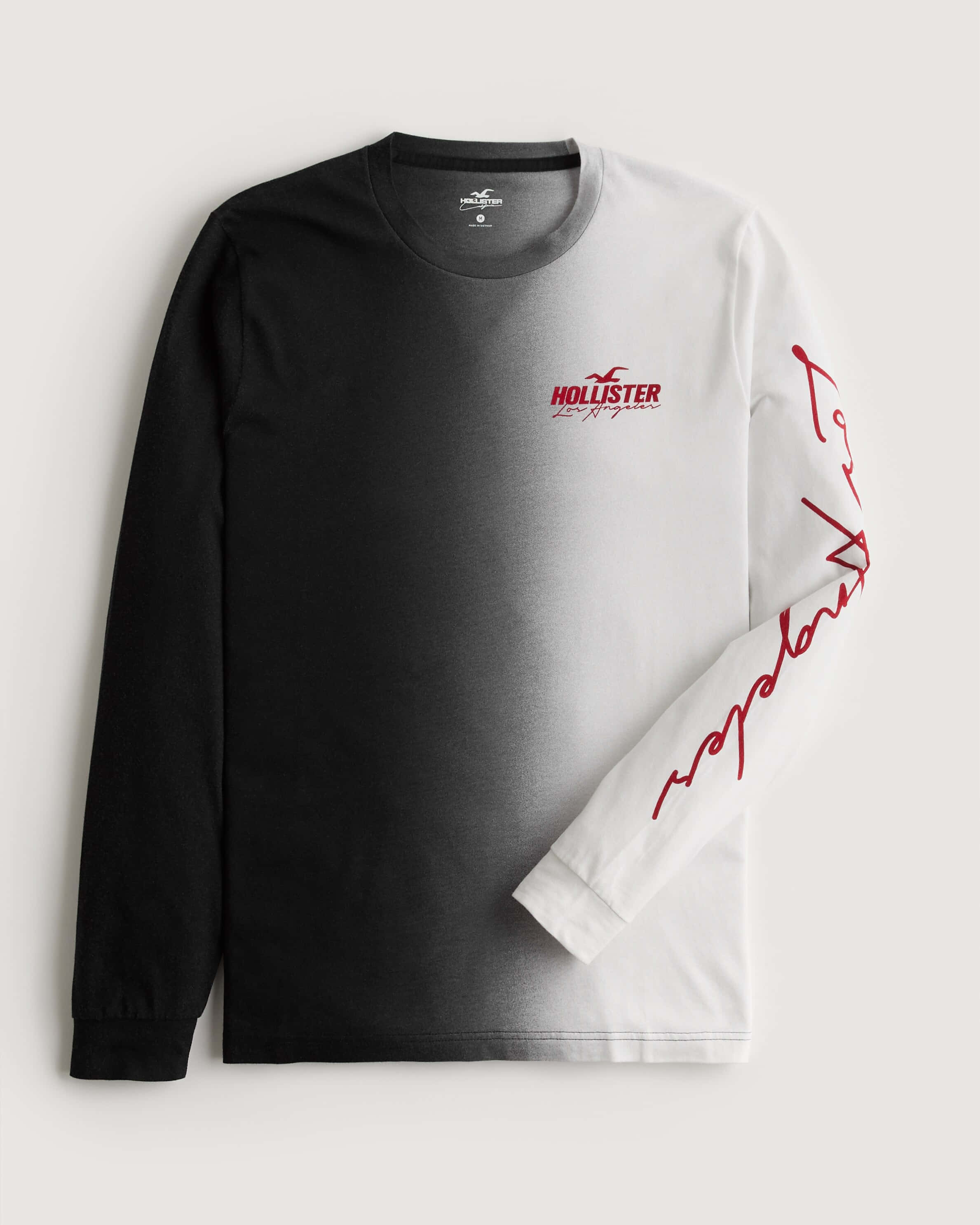 Hollister 桌布 壁紙 — 一件由黑到白漸層的長袖襯衫，袖子上有紅色Hollister標誌和文字，平放在中性背景上展示。