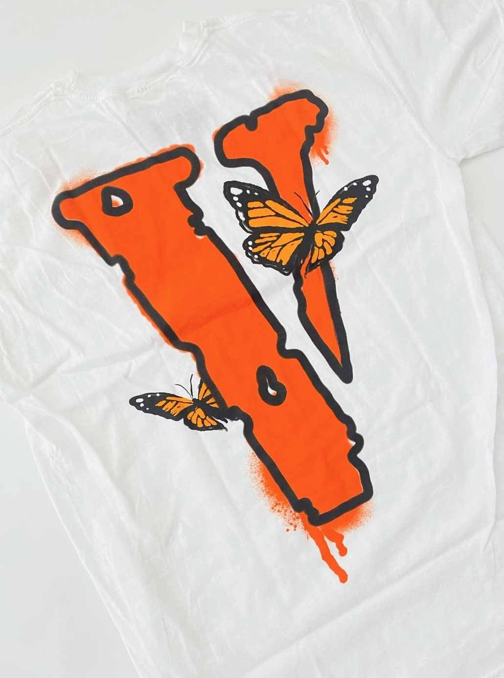 Vlone 桌布 壁紙 — 一件白色T恤上有一個大膽的橙色噴漆V字，兩隻帝王斑蝶棲息在它的曲線上。