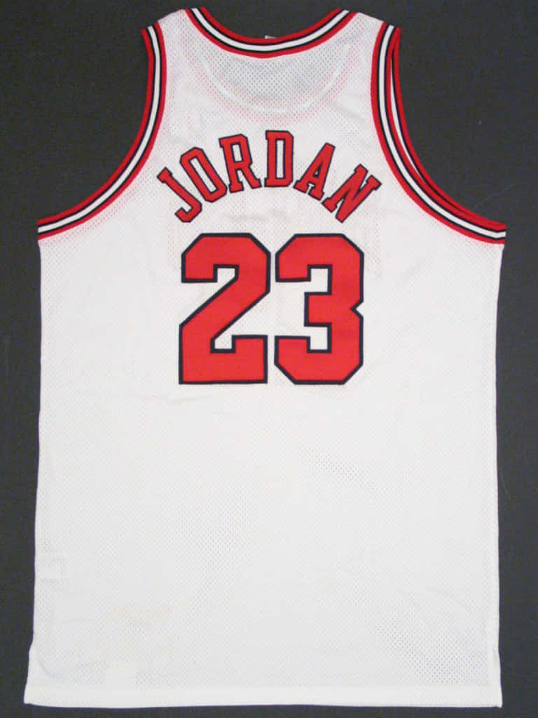 桌布 壁紙 — 一件白色芝加哥公牛隊球衣，帶有紅色 'JORDAN 23' 字樣和紅色鑲邊袖子，在深色背景下展示。