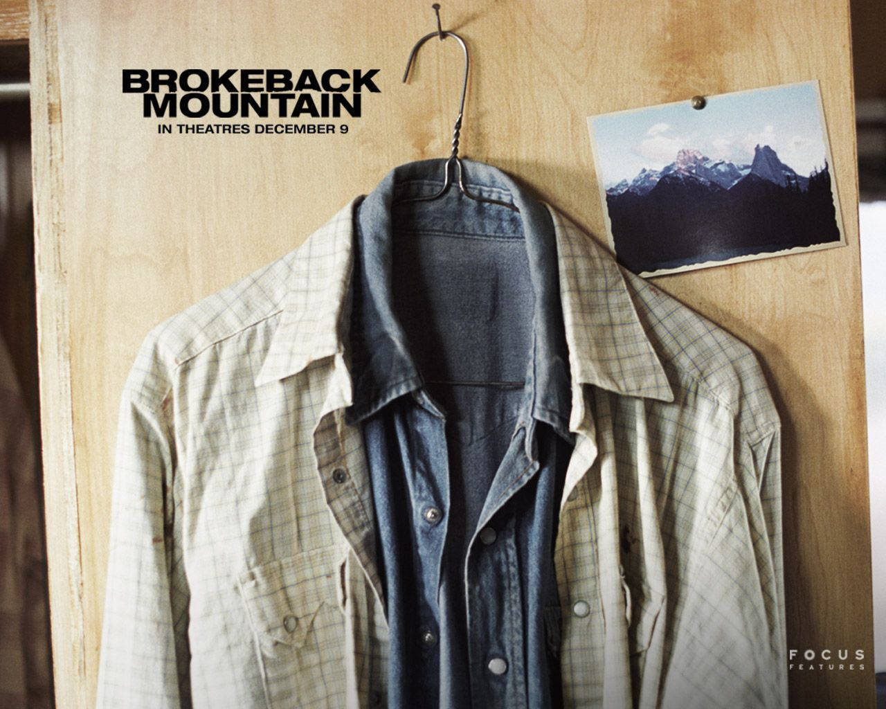 brokeback mountain 桌布 壁紙 — 一件破舊的格紋襯衫掛在掛鉤上，旁邊是木牆上的山景照片和電影標題文字。