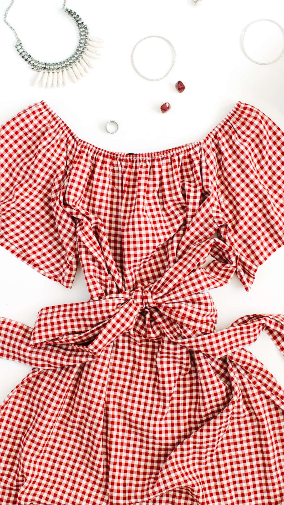 Clothes 桌布 壁紙 — 一件紅白格紋露肩連身裙，腰間繫有蝴蝶結，平放在白色背景上，周圍環繞著珠寶首飾。